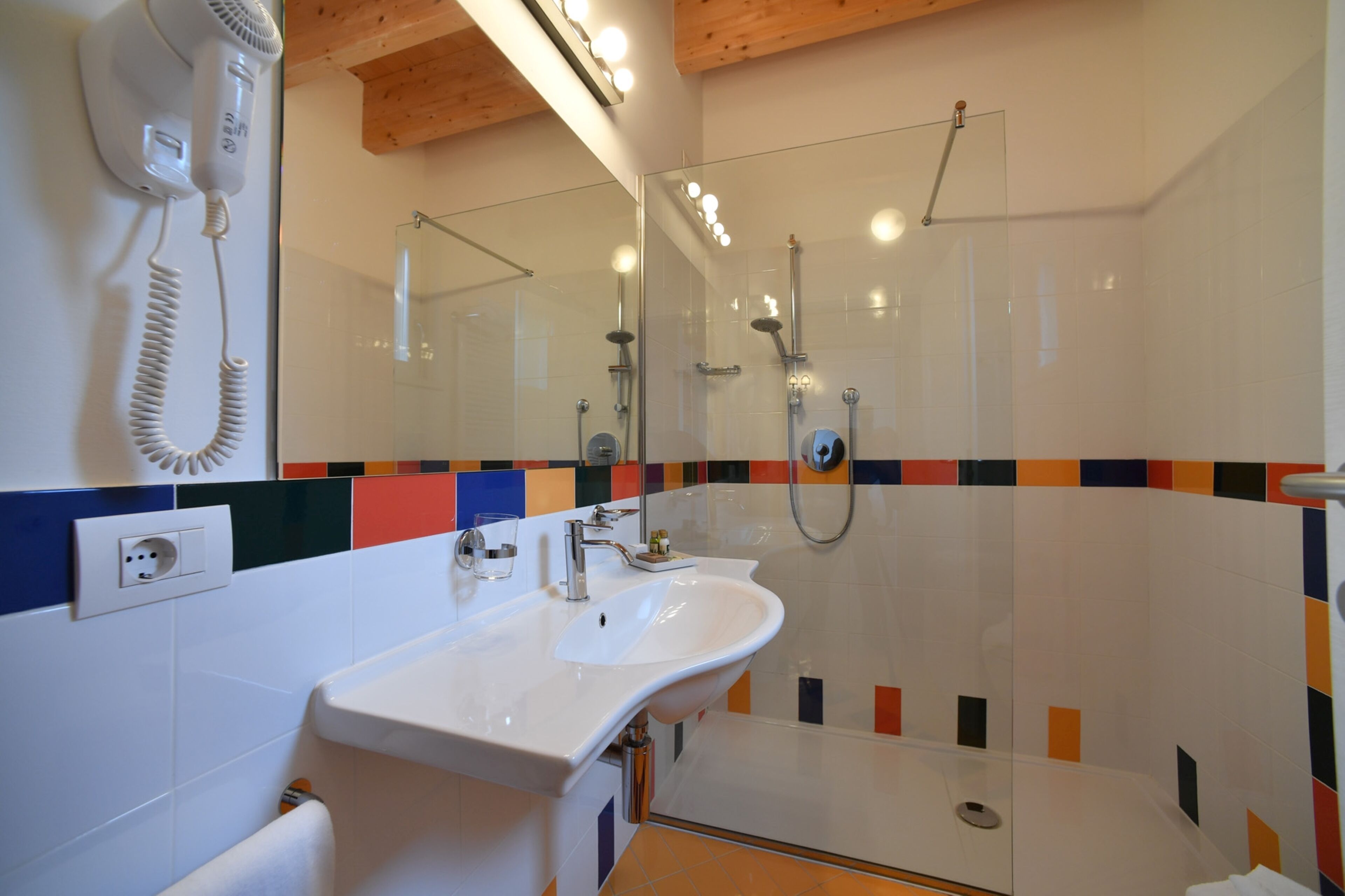 Un baño con un lavabo blanco, una cabina de ducha de vidrio y un espejo sobre el lavabo.