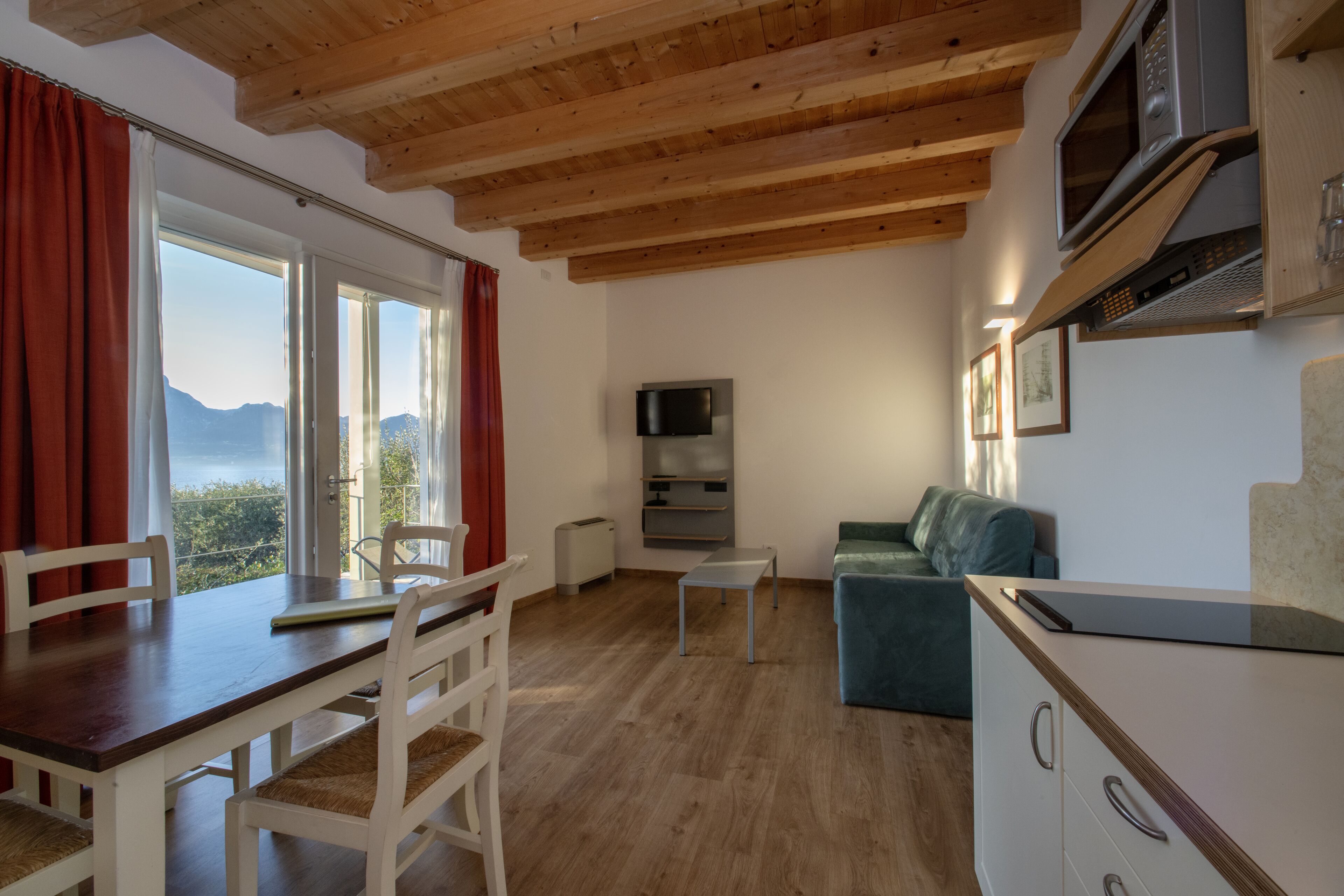 Una sala moderna con techo de madera, una mesa de comedor con sillas, un sofá, un televisor montado en la pared y una zona de cocina con microondas.