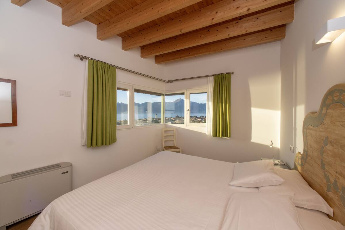 A bedroom with a large bed, a chair, and a view of mountains through the windows.