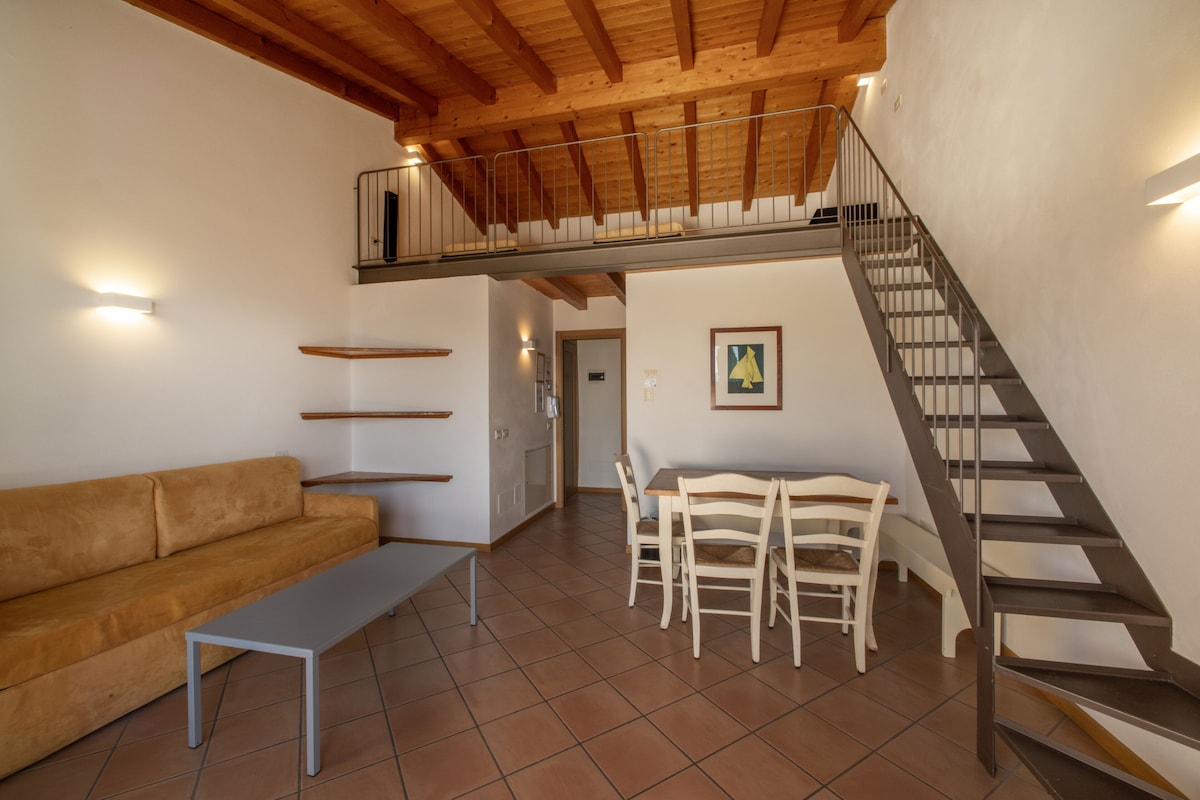 Un vaste espace de vie doté d’un haut plafond, d’un escalier en bois, d’un canapé, d’une table à manger avec des chaises et d’un petit balcon.