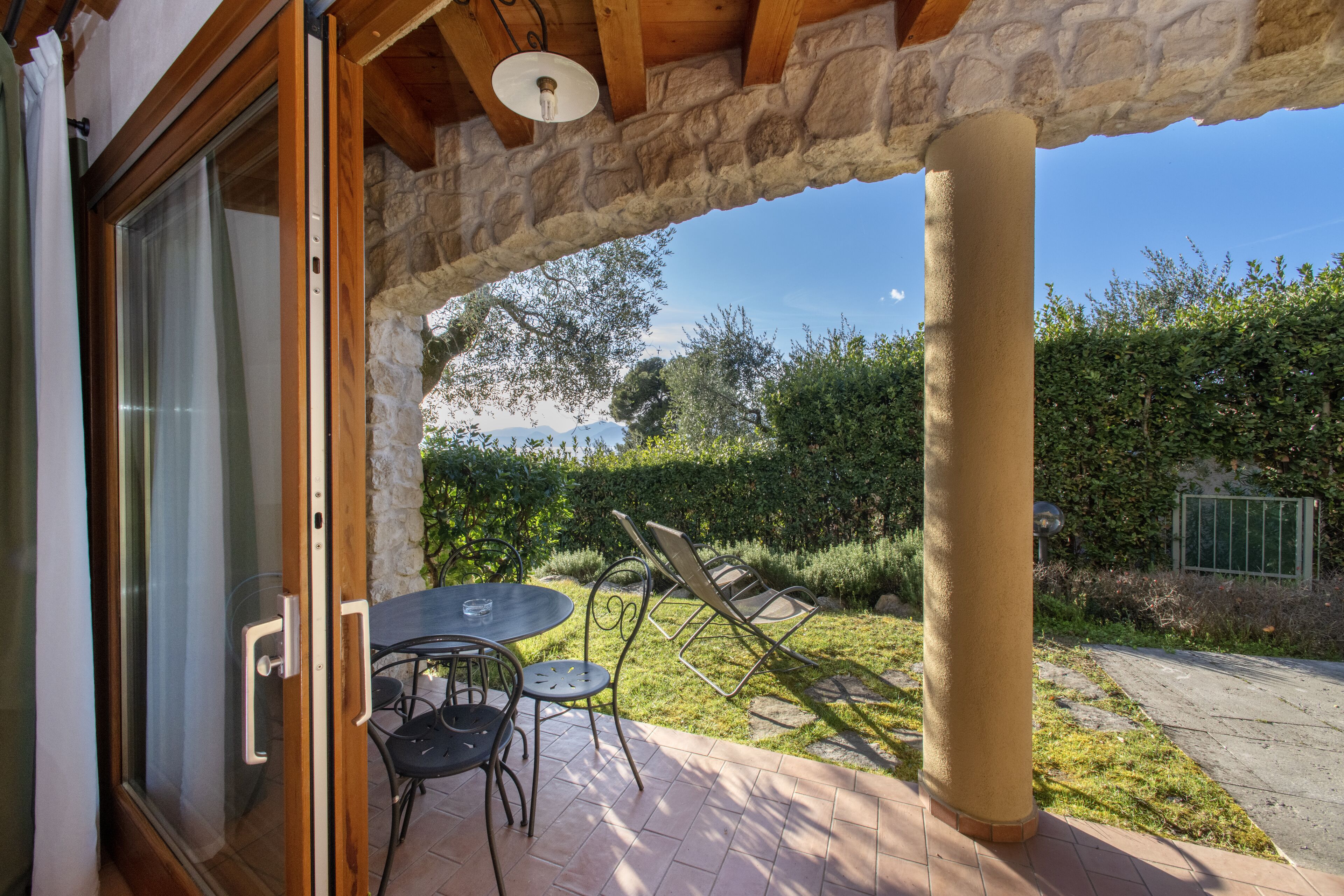 An outdoor patio with a table and chairs, stone pillars, and a view of a garden and mountains.