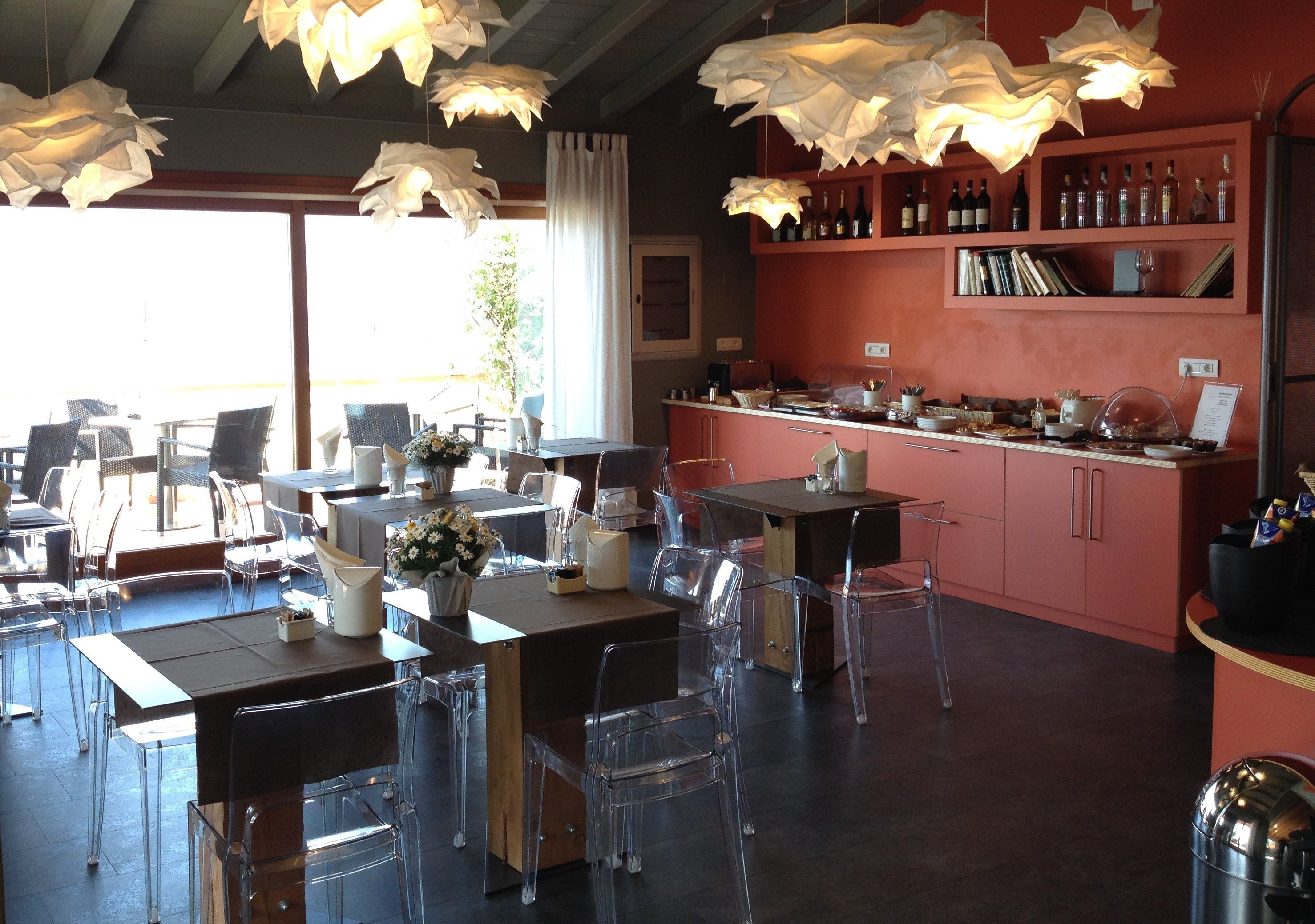 A restaurant interior with clear glass chairs, wooden tables, and hanging paper lamps.
