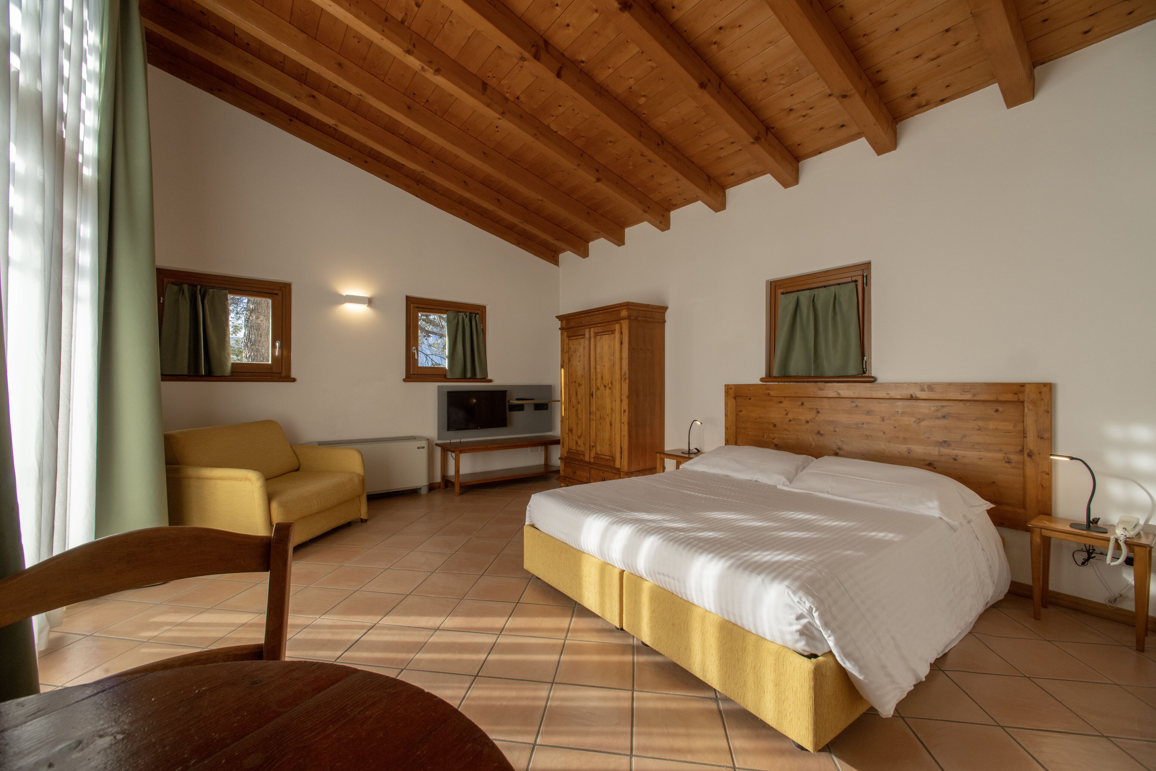 Ein Schlafzimmer mit einem großen Bett, einem Holz-Kopfteil, einem Schrank aus Holz, einem kleinen Tisch, einem Fernseher und einem Sofa.