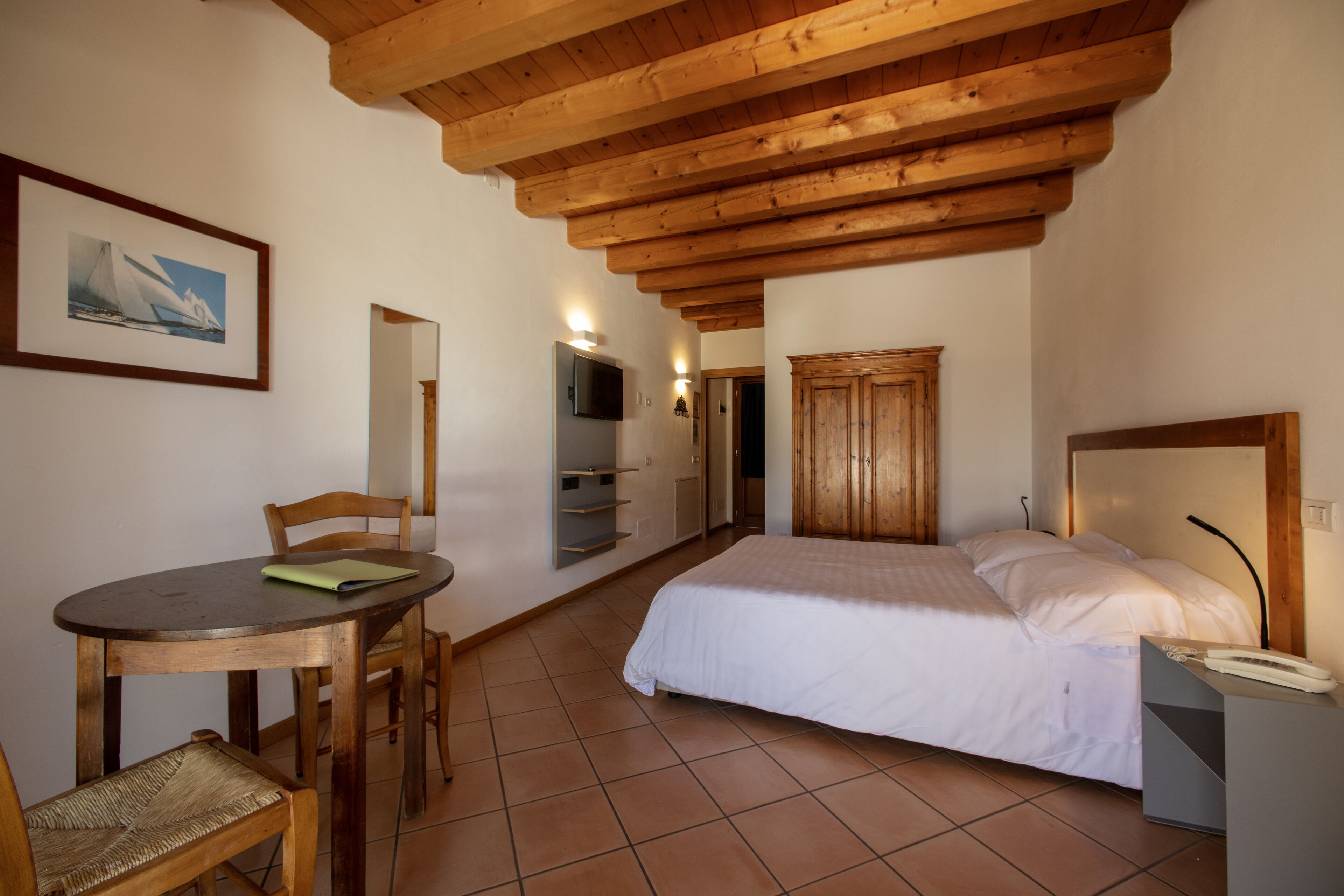 Un dormitorio con techo de madera, una cama, un escritorio con sillas, un televisor y un armario.