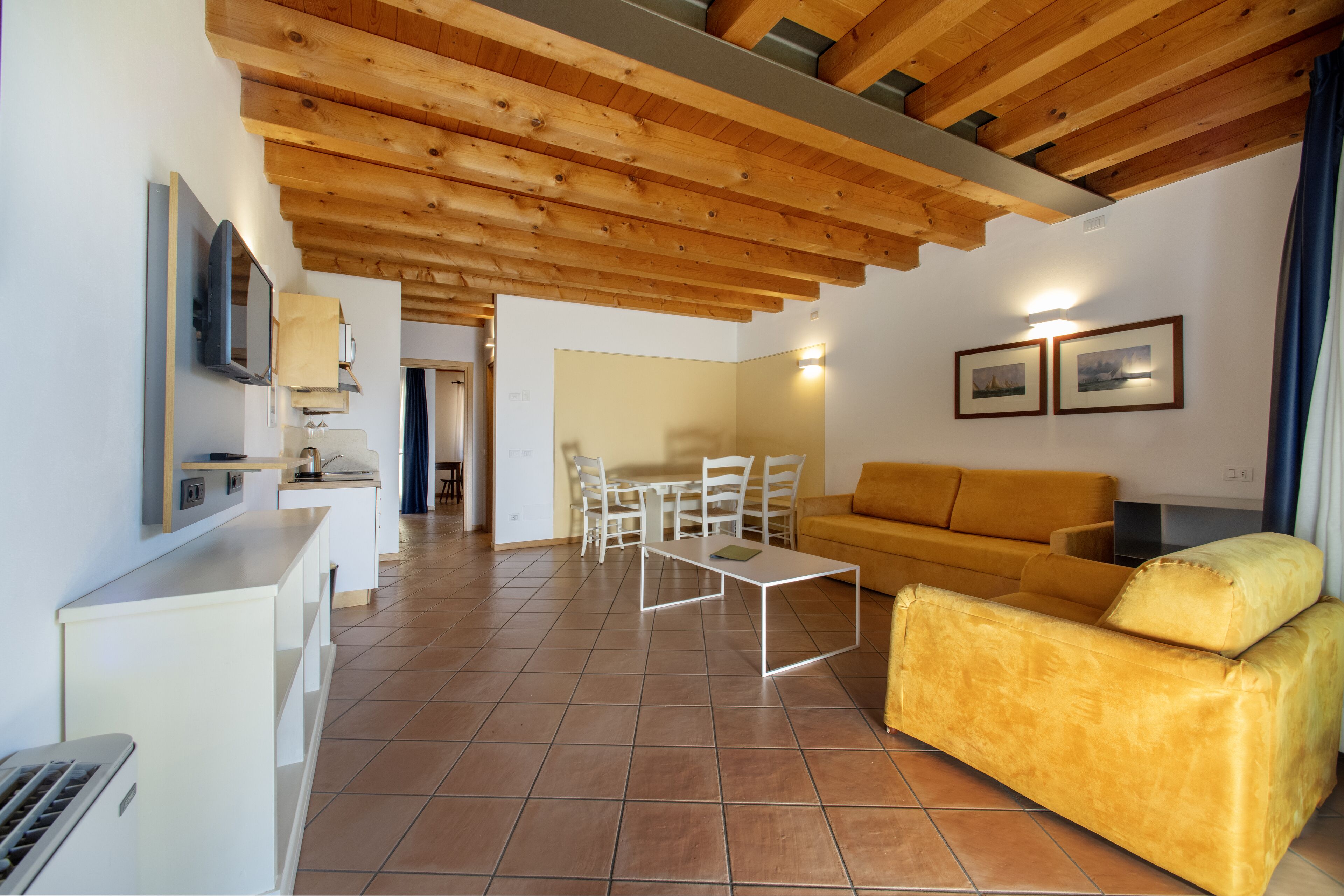 Amplia sala de estar con techo de madera, un sofá amarillo, una mesa de centro blanca y un juego de comedor.
