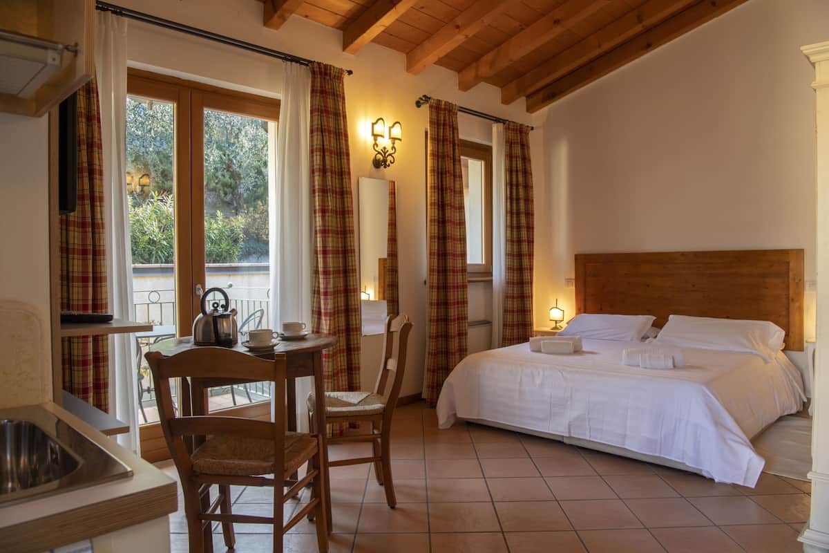 A bedroom with a large bed, a wooden headboard, a bedside table with a kettle, and a chair.
