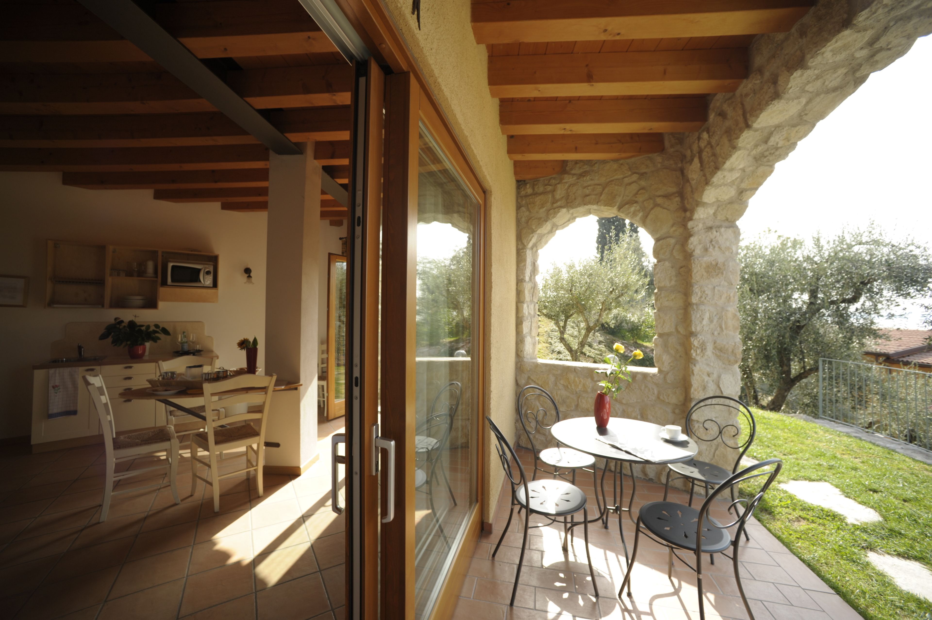 A dining area with a table and chairs, a kitchen with a microwave, and a view of a garden through a glass door.