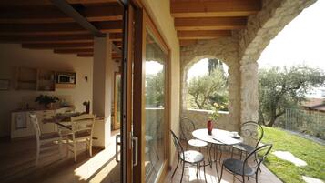 A dining area with a table and chairs, a kitchen with a microwave, and a view of a garden through a glass door.