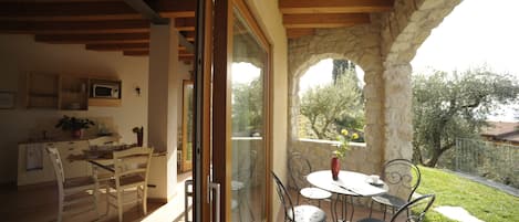 A dining area with a table and chairs, a kitchen with a microwave, and a view of a garden through a glass door.