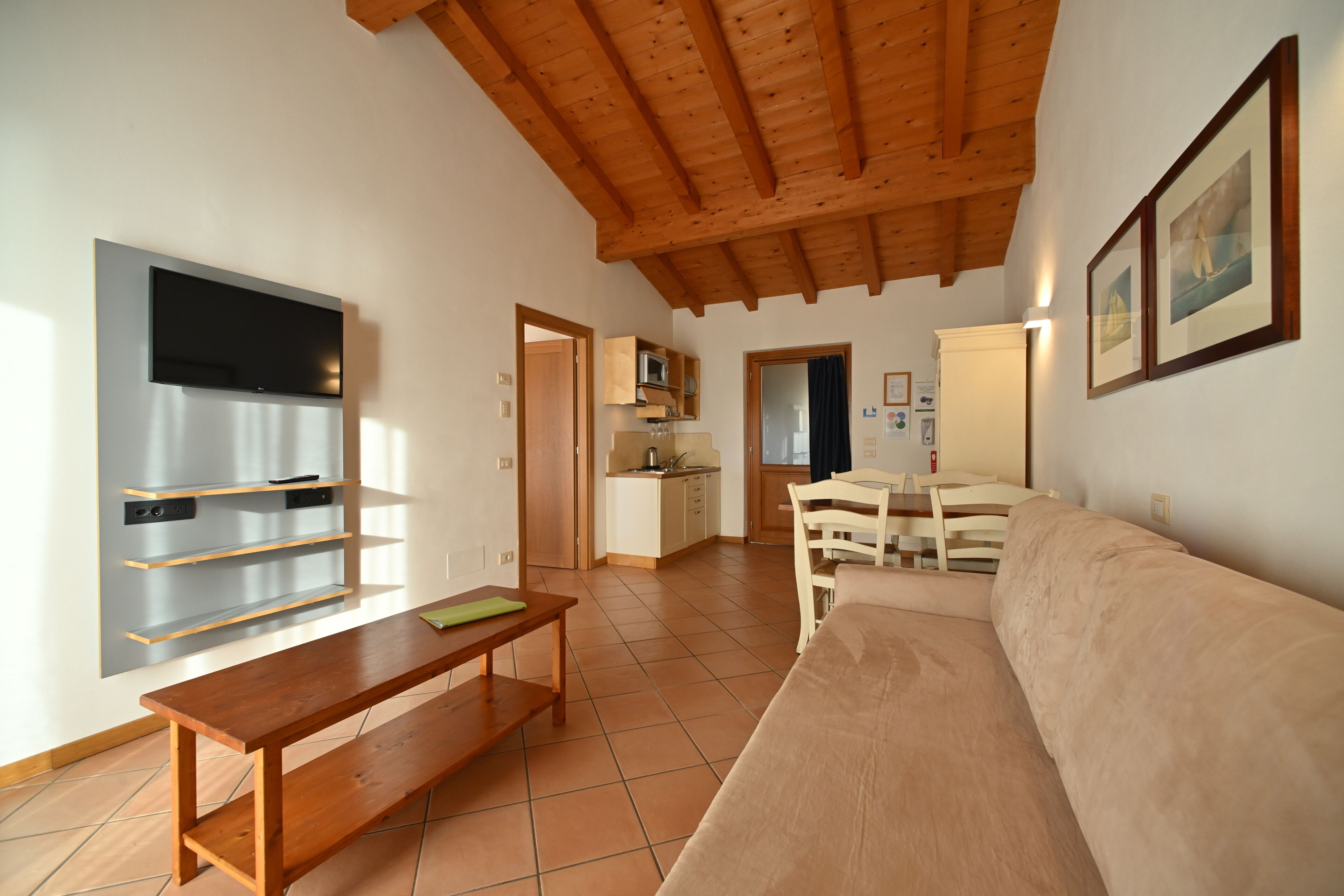 Een moderne woonkamer met een houten plafond, een flatscreen televisie, een bank, een eettafel met stoelen en een keuken op de achtergrond.