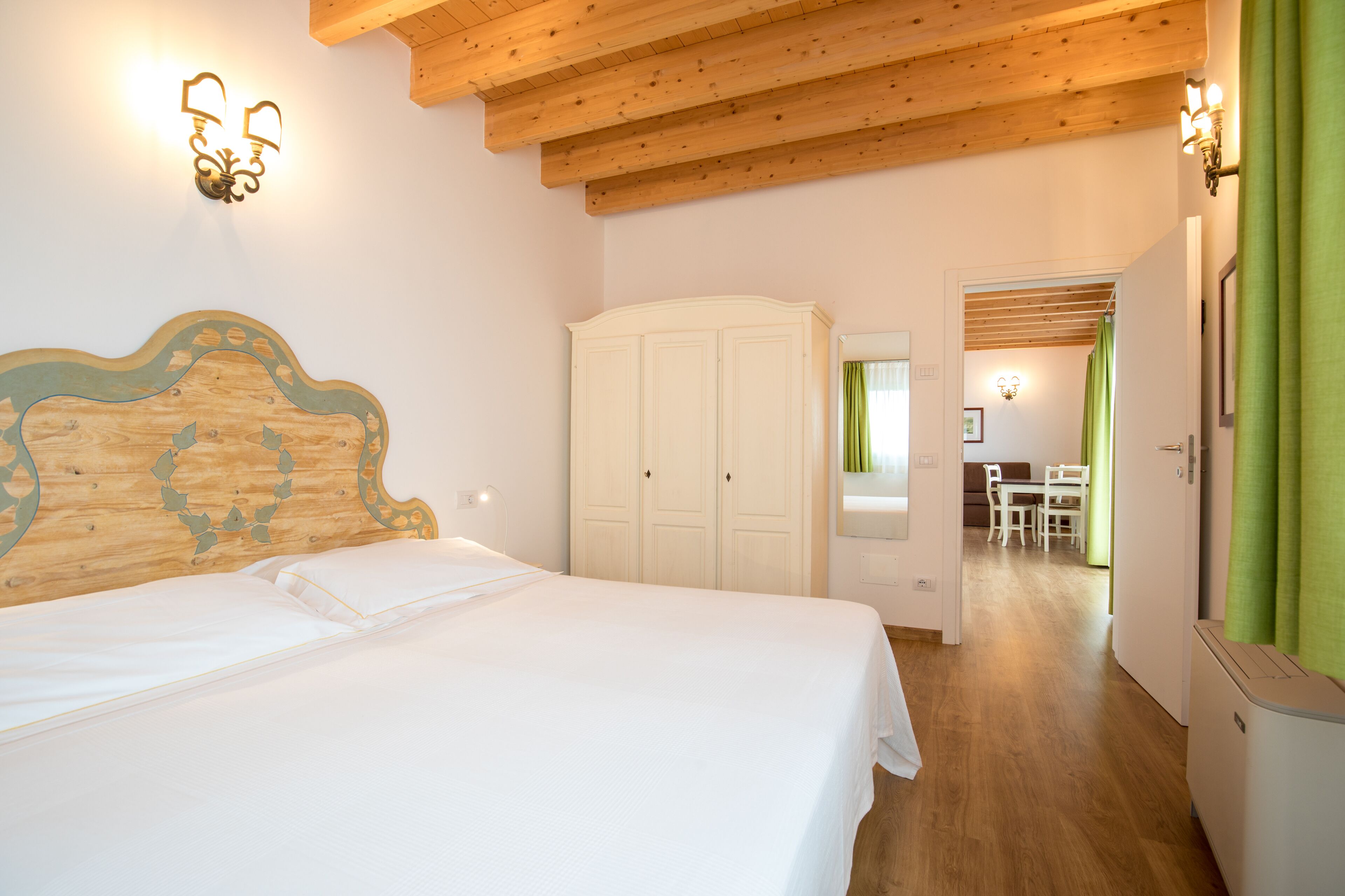 A bedroom with a wooden headboard, a white bed, a wardrobe, and a bathroom visible through an open door.