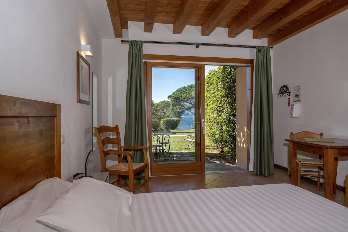 A bedroom with a bed, a wooden headboard, a chair, a table, and a sliding glass door leading to an outdoor area with a table and chairs.