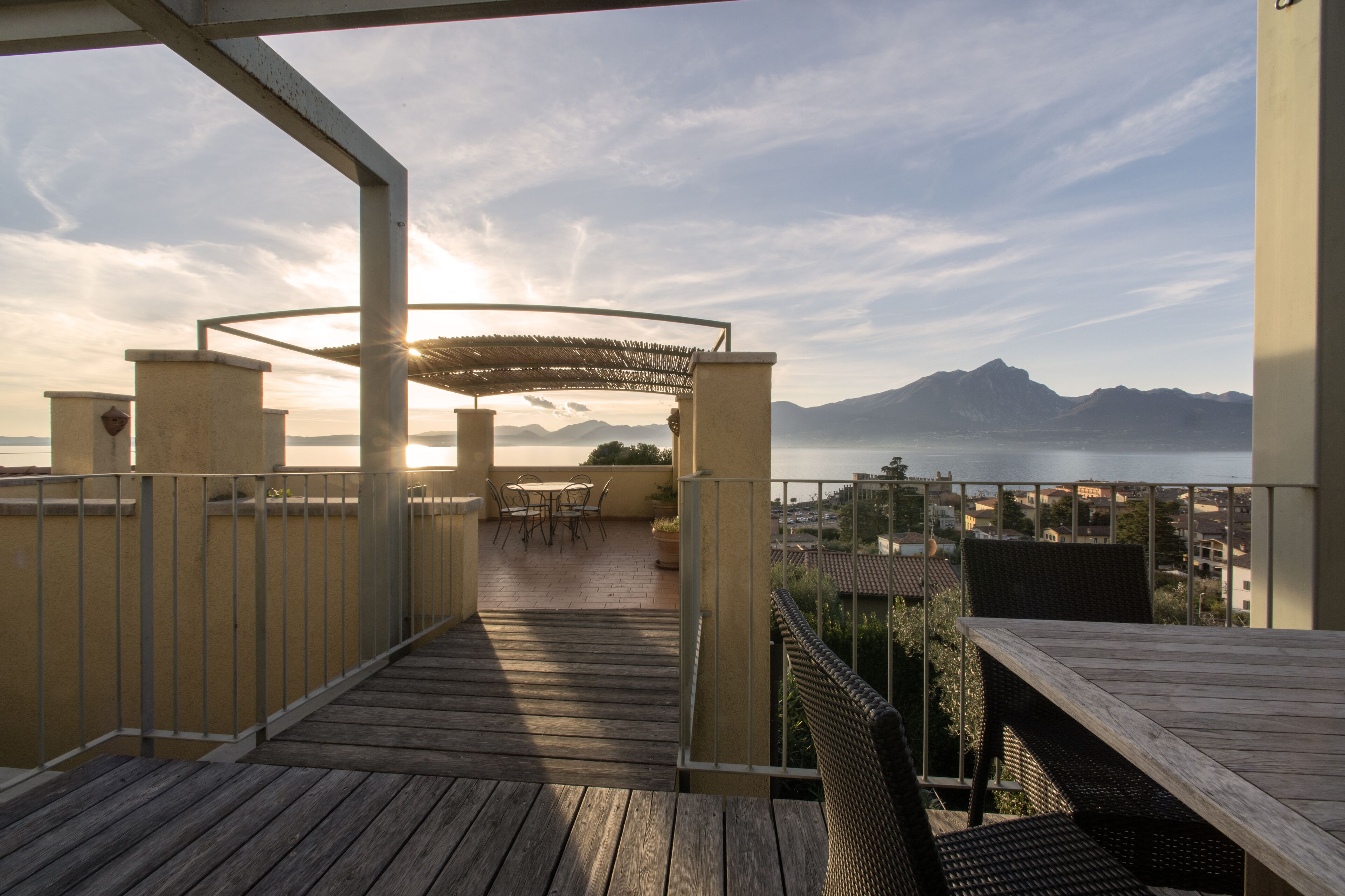 A wooden deck with outdoor furniture, a pergola, and a view of a mountain range and body of water.