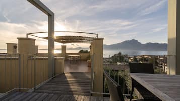 A wooden deck with outdoor furniture, a pergola, and a view of a mountain range and body of water.