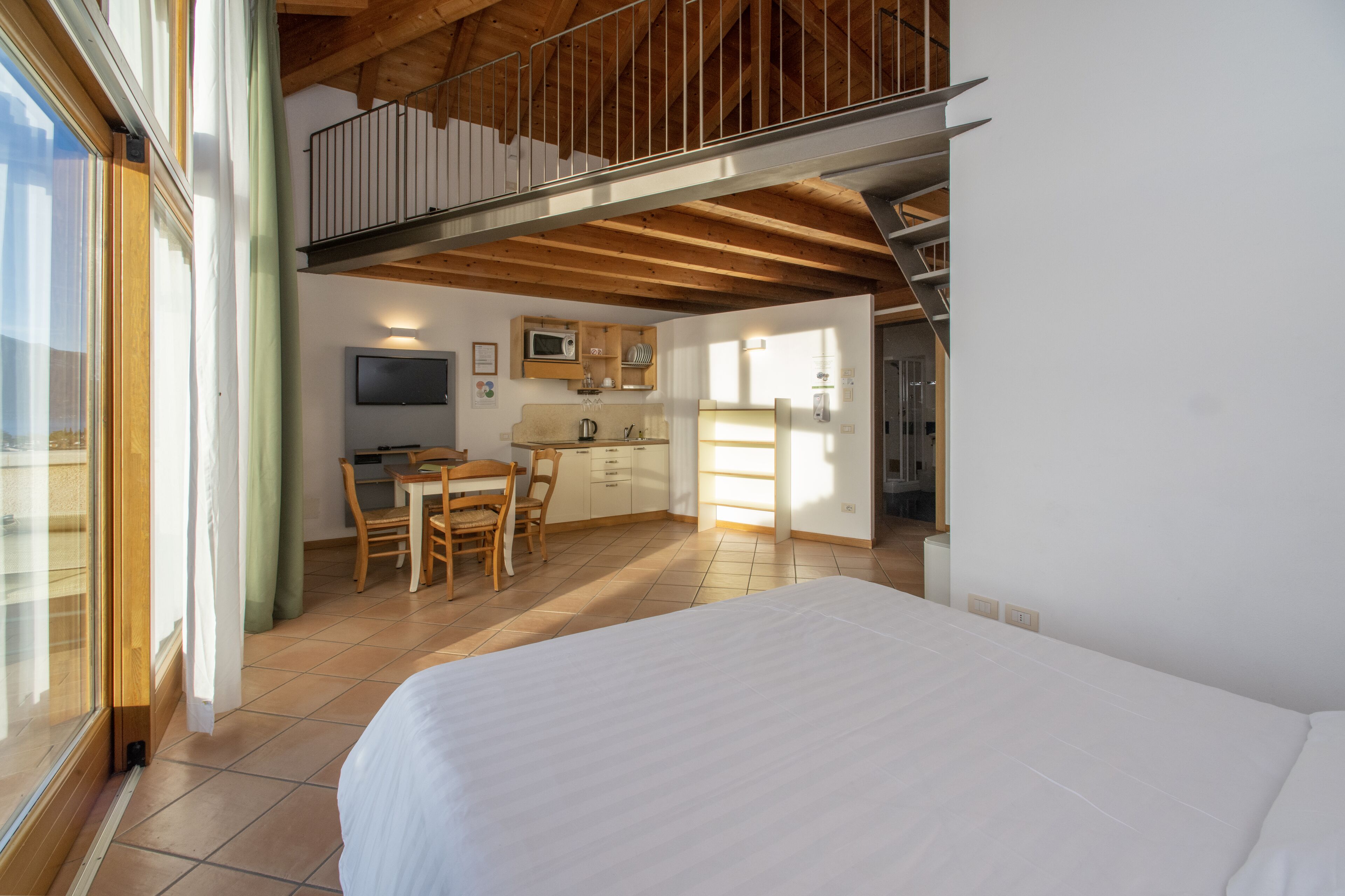 A bedroom with a large bed, a dining area with a table and chairs, a kitchenette, and a TV.