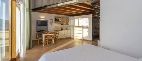 A bedroom with a large bed, a dining area with a table and chairs, a kitchenette, and a TV.