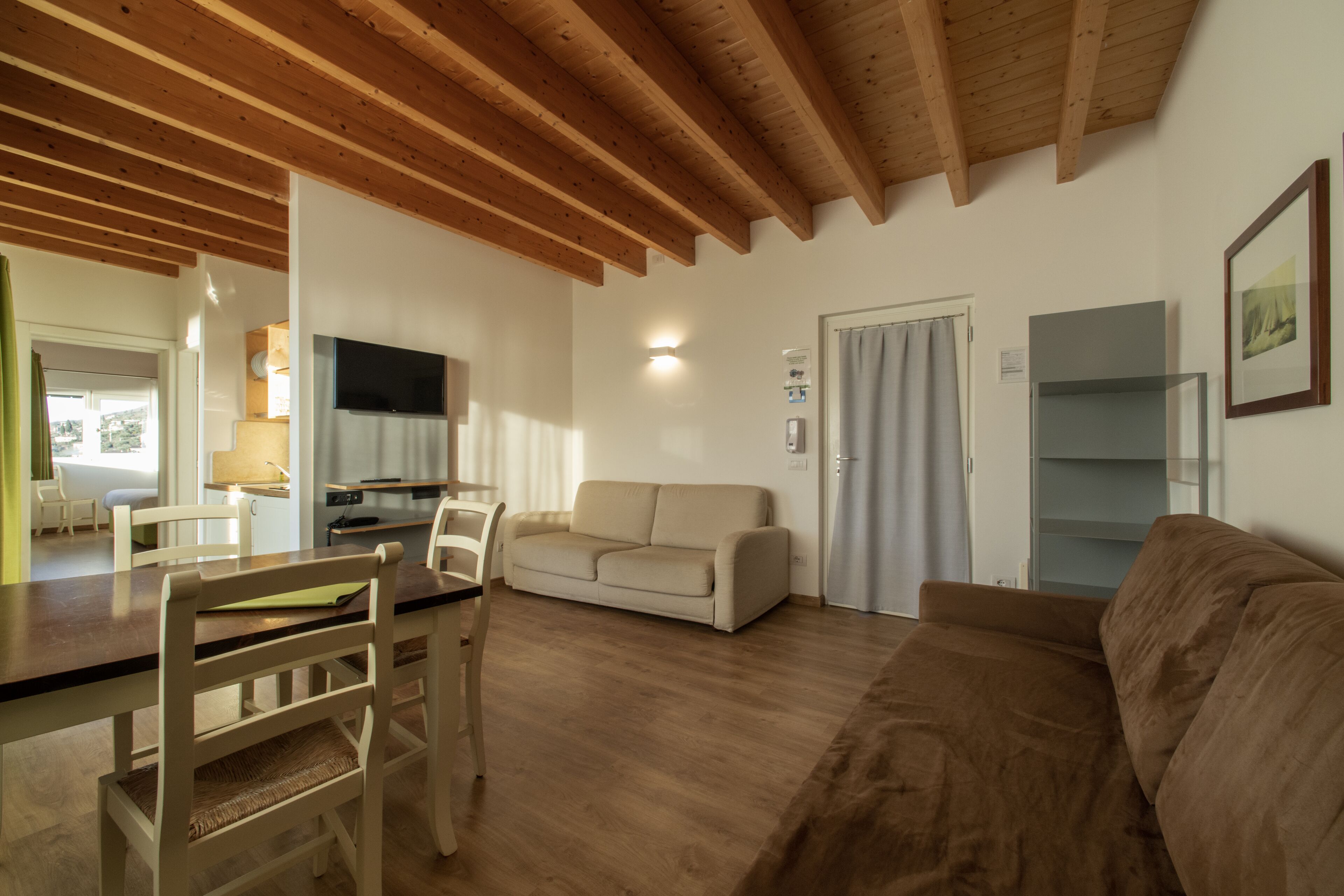 A living room with wooden beams, a sofa, a couch, a TV, and a dining area with chairs and a table.
