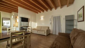 A living room with wooden beams, a sofa, a couch, a TV, and a dining area with chairs and a table.