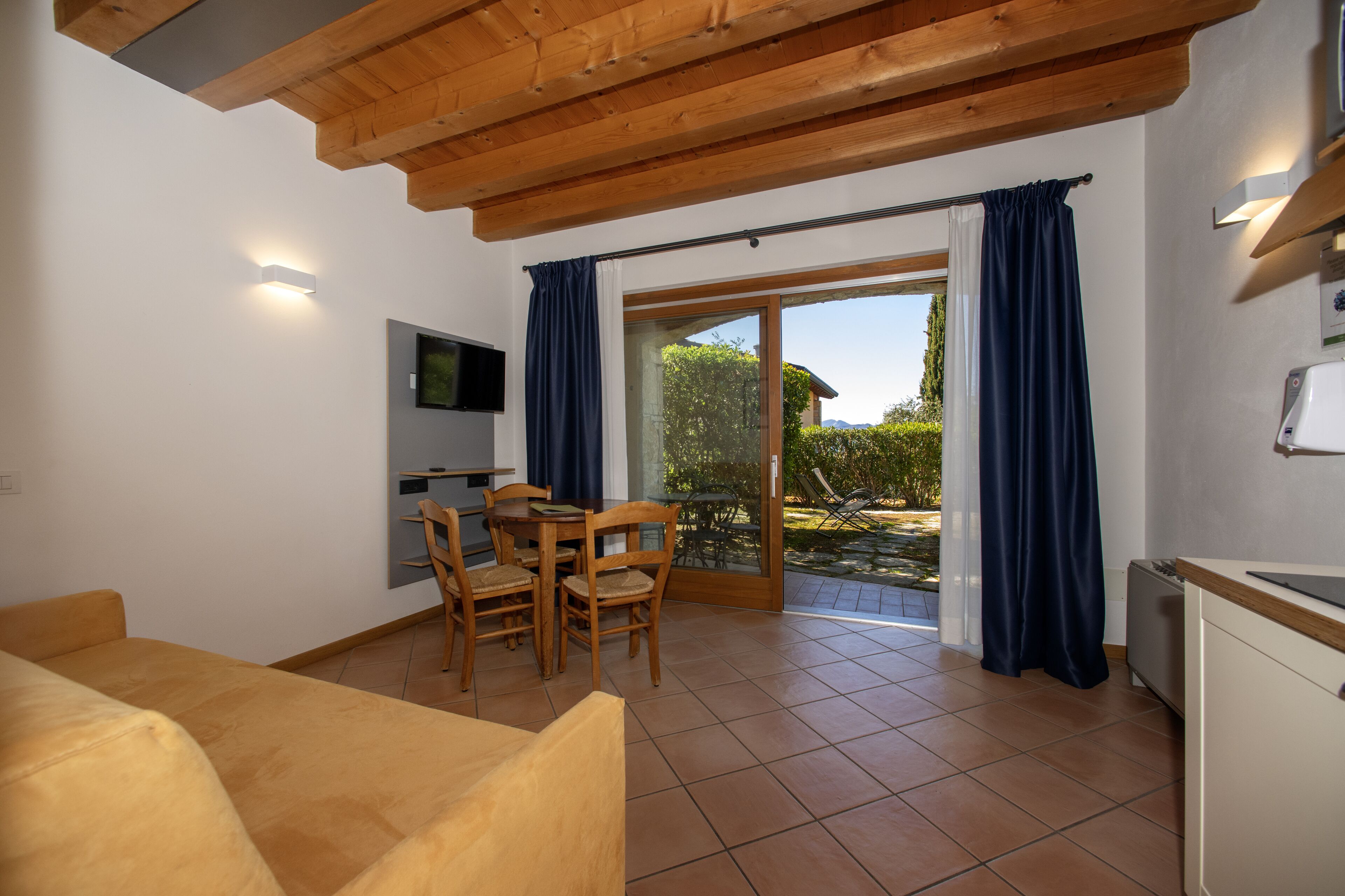 A compact living space with a dining area, a TV mounted on the wall, and a sliding glass door leading to an outdoor area.