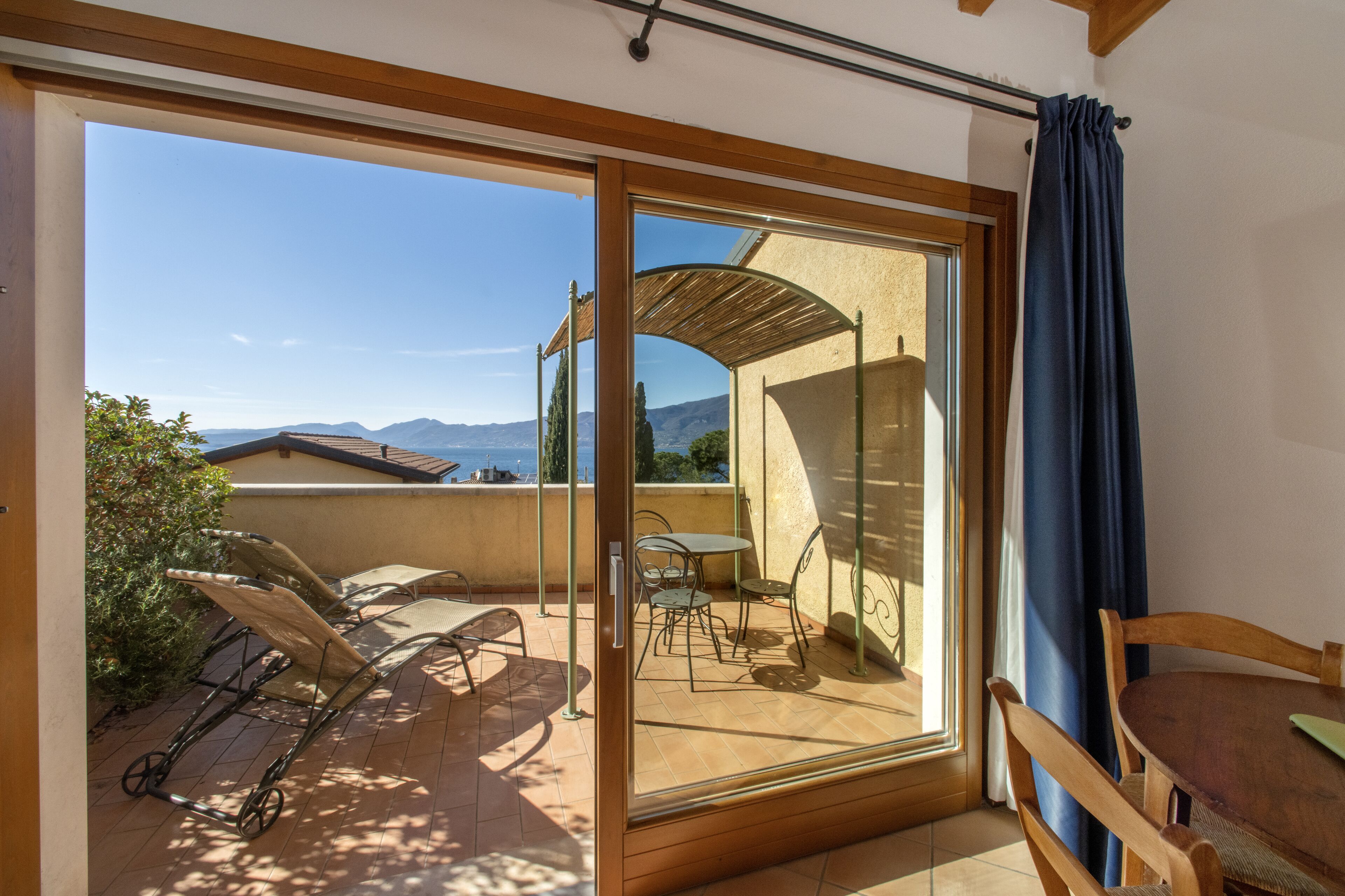 Een balkon met een tafel en stoelen, een houten pergola en uitzicht op bergen.