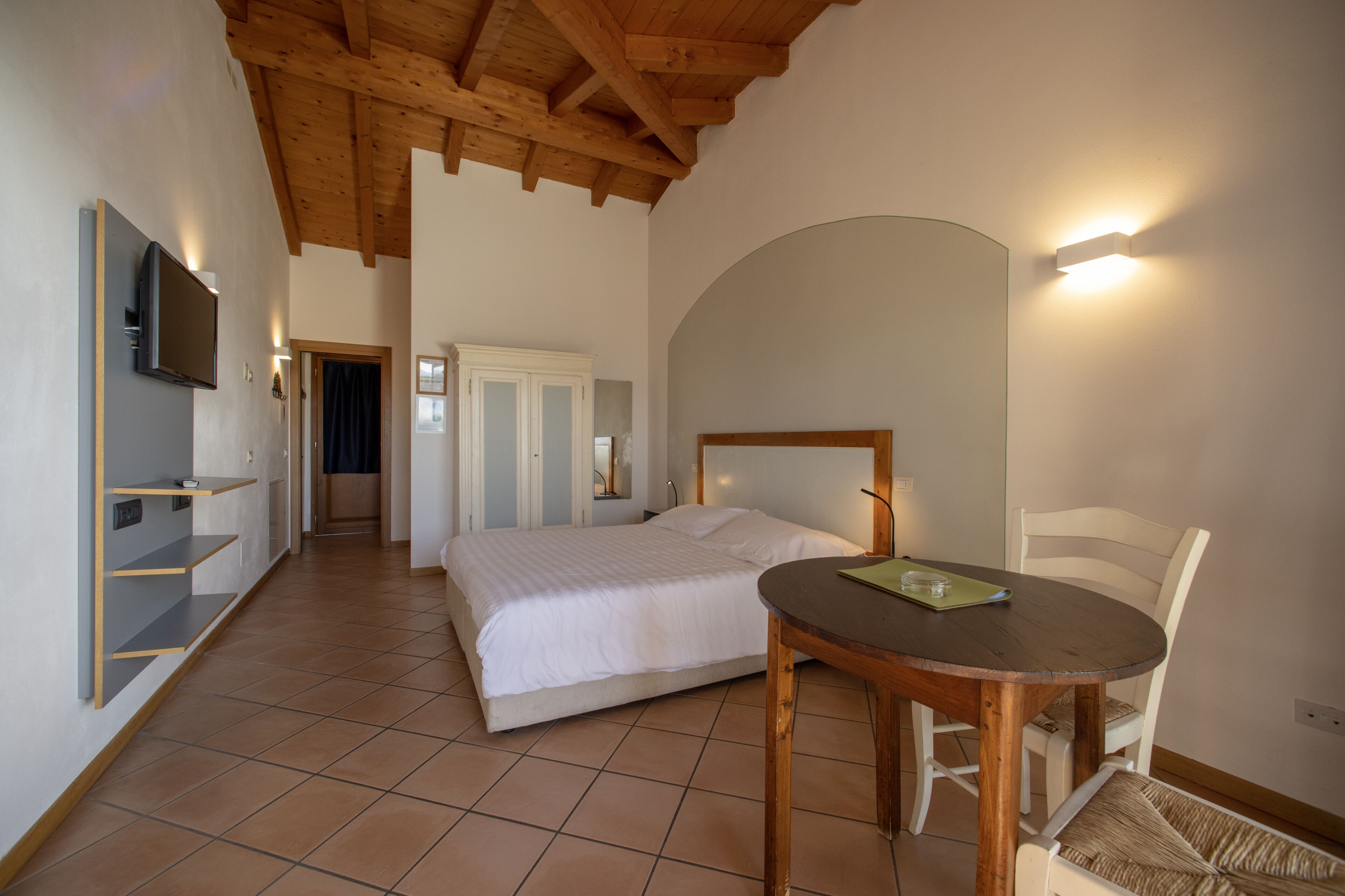 Ein Schlafzimmer mit Bett, Holzboden, einem an der Wand befestigten Fernseher und einem kleinen Tisch mit Stuhl.