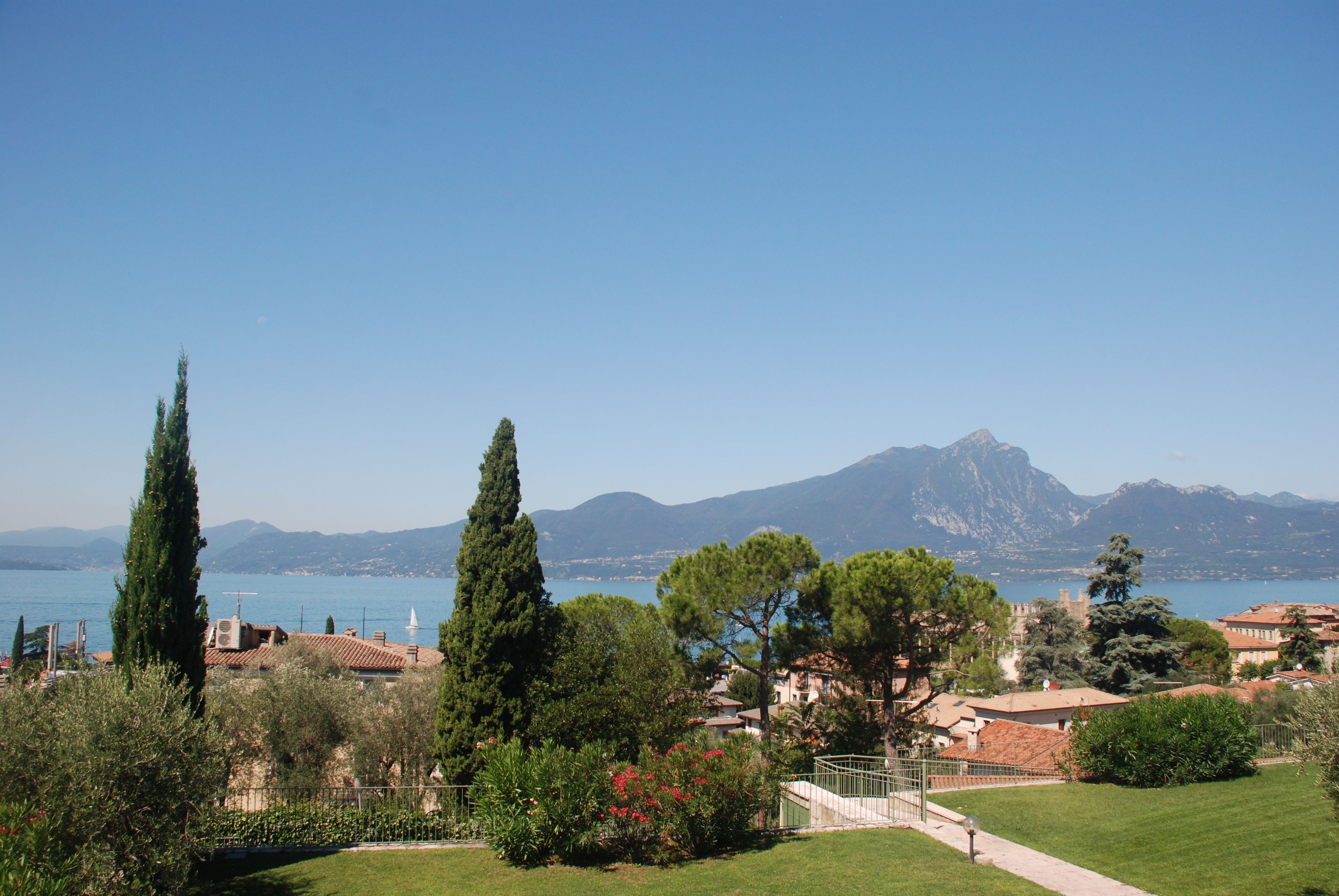 Un paysage côtier offrant une vue dégagée sur la mer, les montagnes et un sentier menant à un bâtiment doté d’un toit en tuiles.