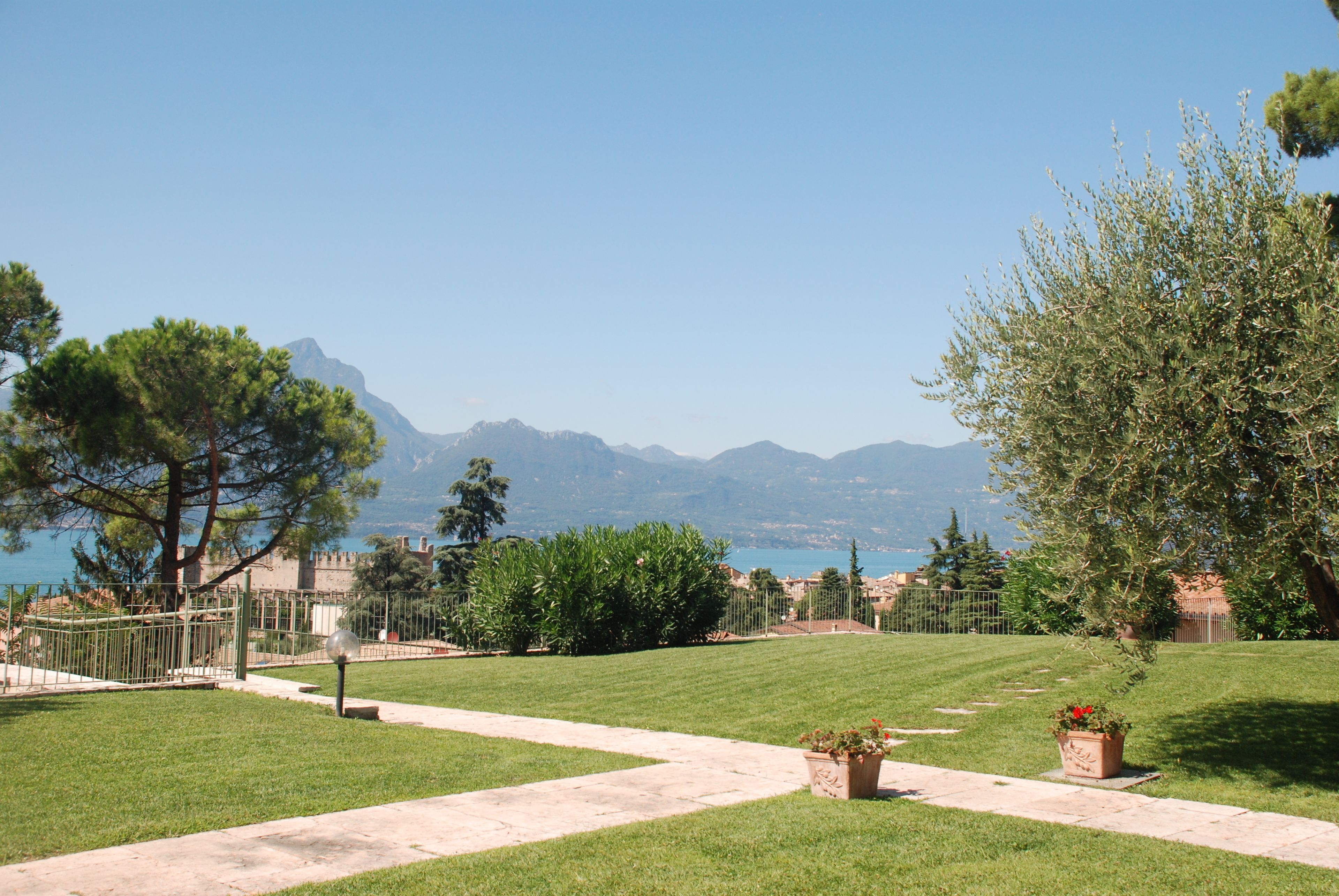 A well-maintained grassy area with a paved pathway, surrounded by trees and a view of distant mountains.