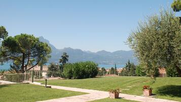 A well-maintained grassy area with a paved pathway, surrounded by trees and a view of distant mountains.