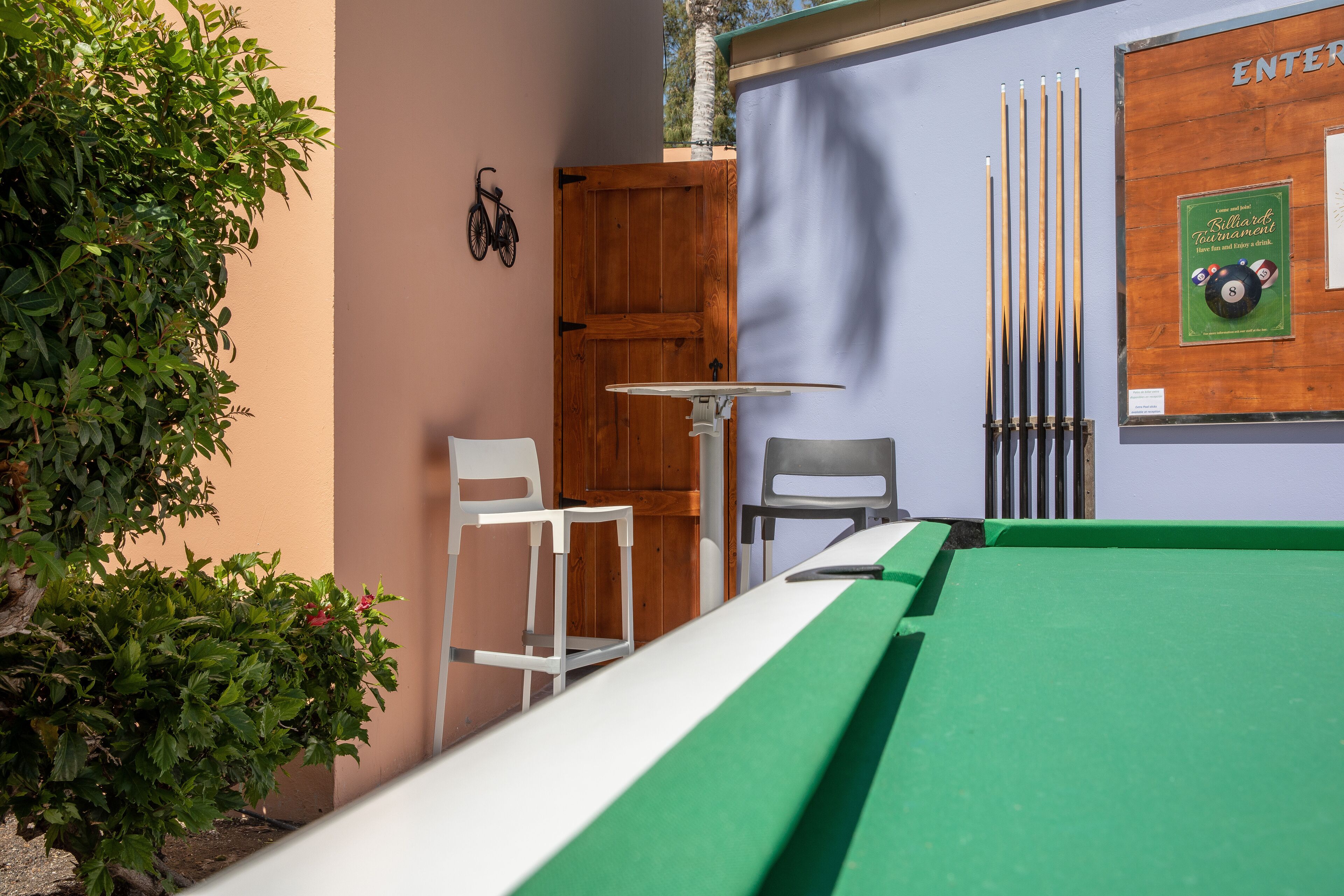 Een pooltafel met een groene viltkleed, een houten deur en twee stoelen.
