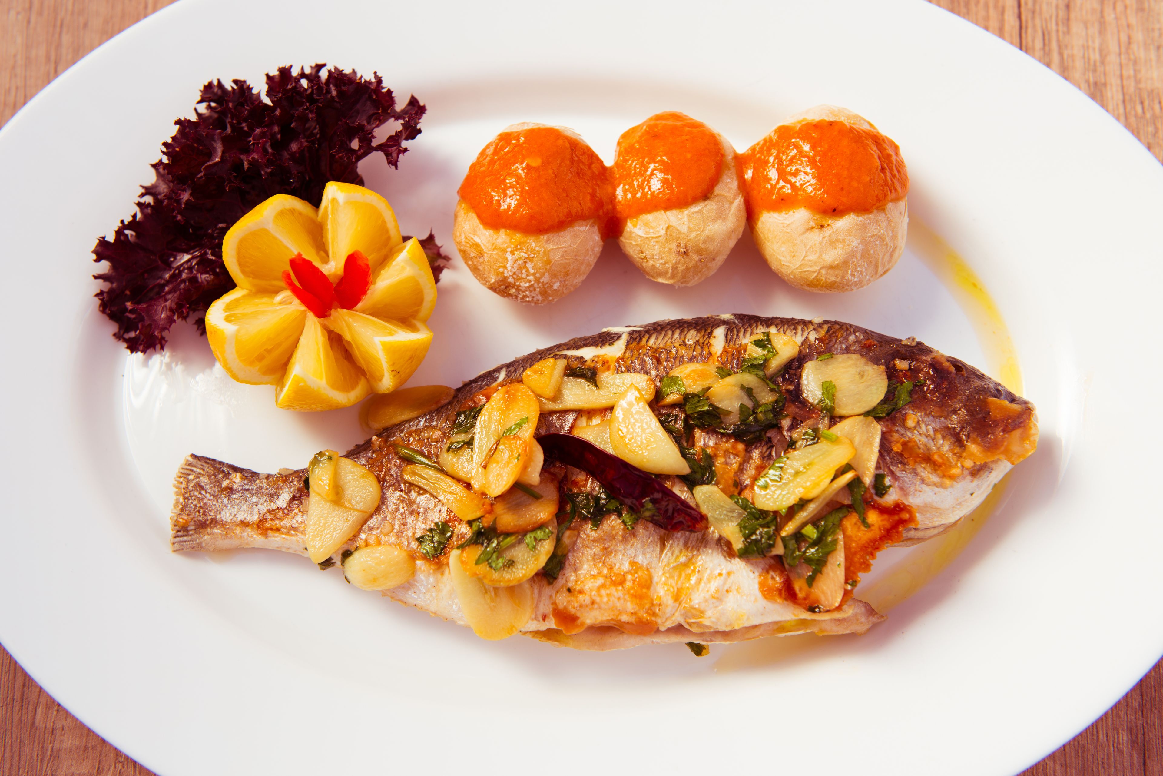 Ein Teller mit Fisch, Zitronenscheiben und einer Zierblume.
