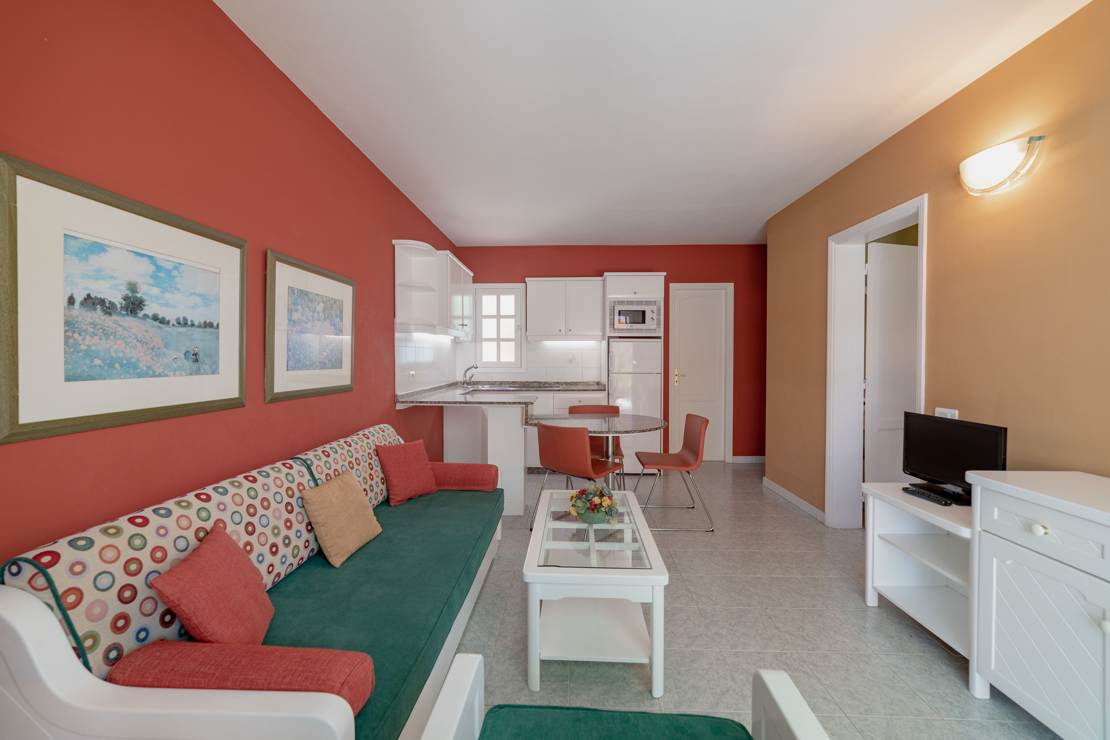 A compact living space with a sofa, a coffee table, a television, and a kitchenette area.