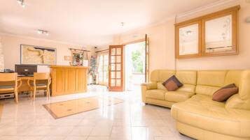 A spacious living area with a yellow leather sofa, a wooden desk with chairs, and a large window providing natural light.