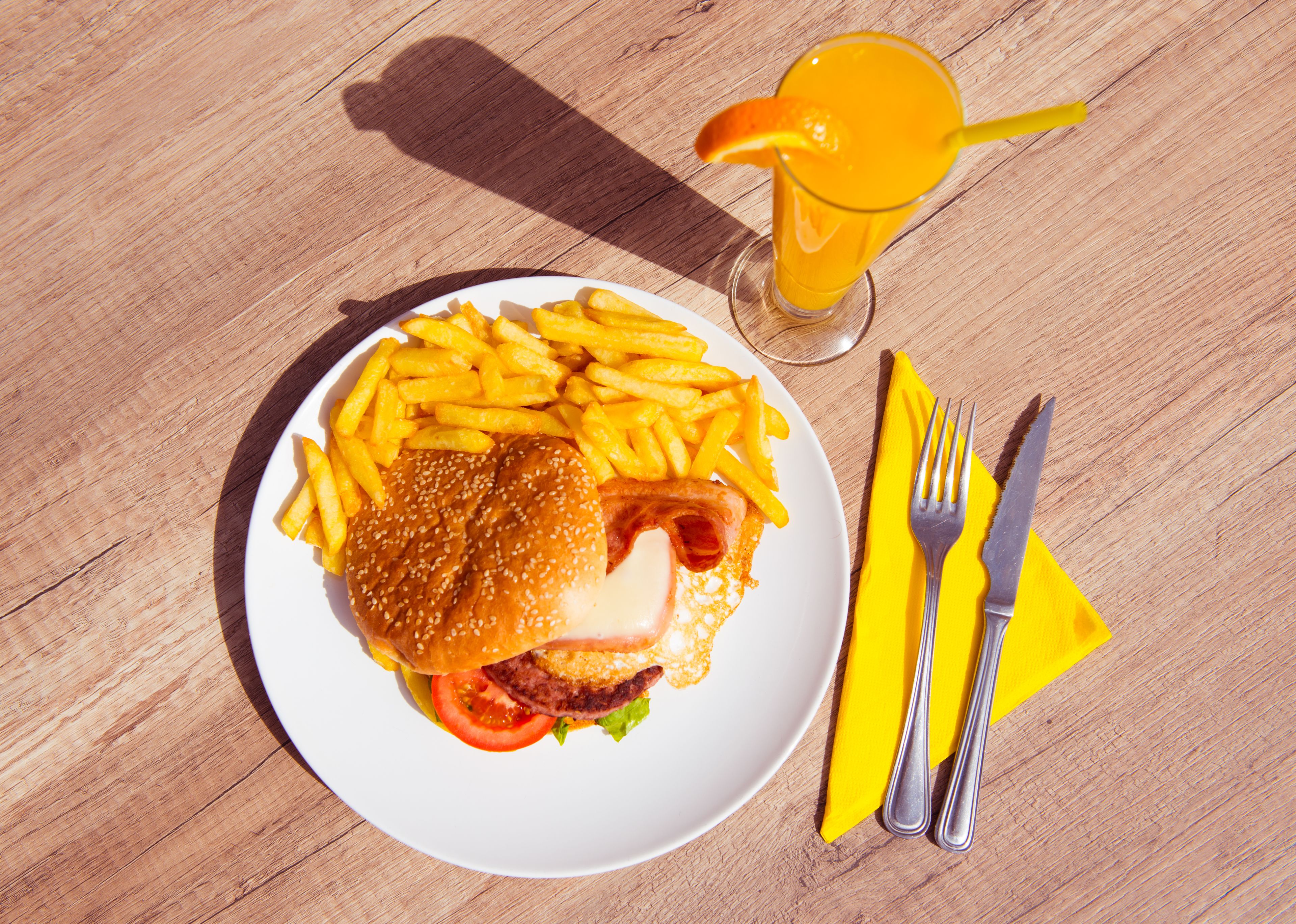 Une assiette de nourriture comprenant des frites, un hamburger et un verre de jus d’orange, le tout posé sur une table en bois.