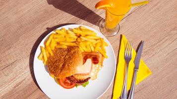Une assiette de nourriture comprenant des frites, un hamburger et un verre de jus d’orange, le tout posé sur une table en bois.