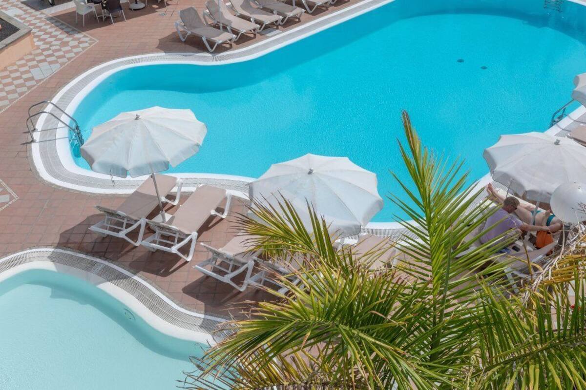 Ein Schwimmbecken mit Liegestühlen und Sonnenschirmen, umgeben von einer gefliesten Terrasse.