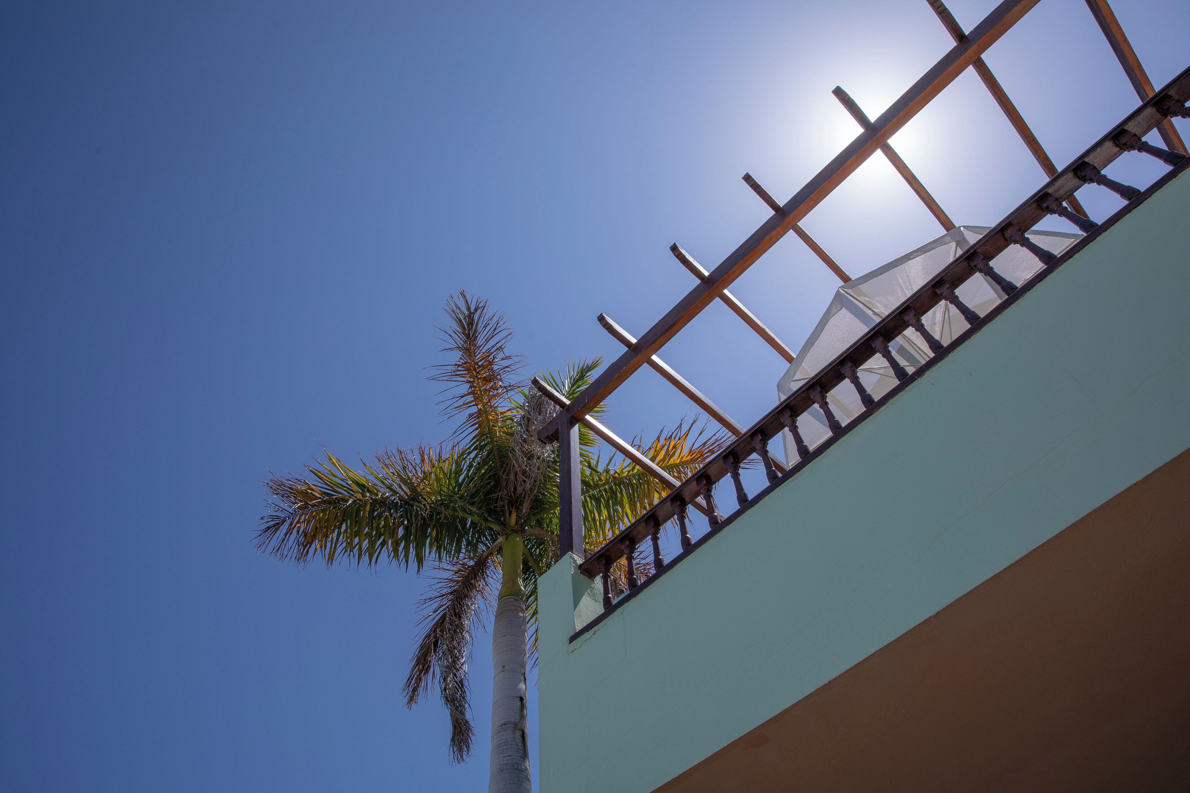 Un edificio con un balcón, una palmera y un cielo azul despejado.