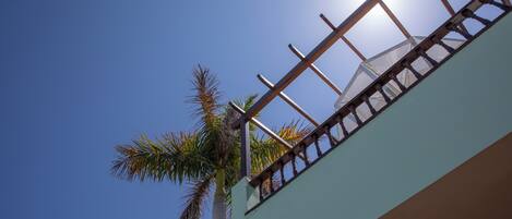 Un edificio con un balcón, una palmera y un cielo azul despejado.