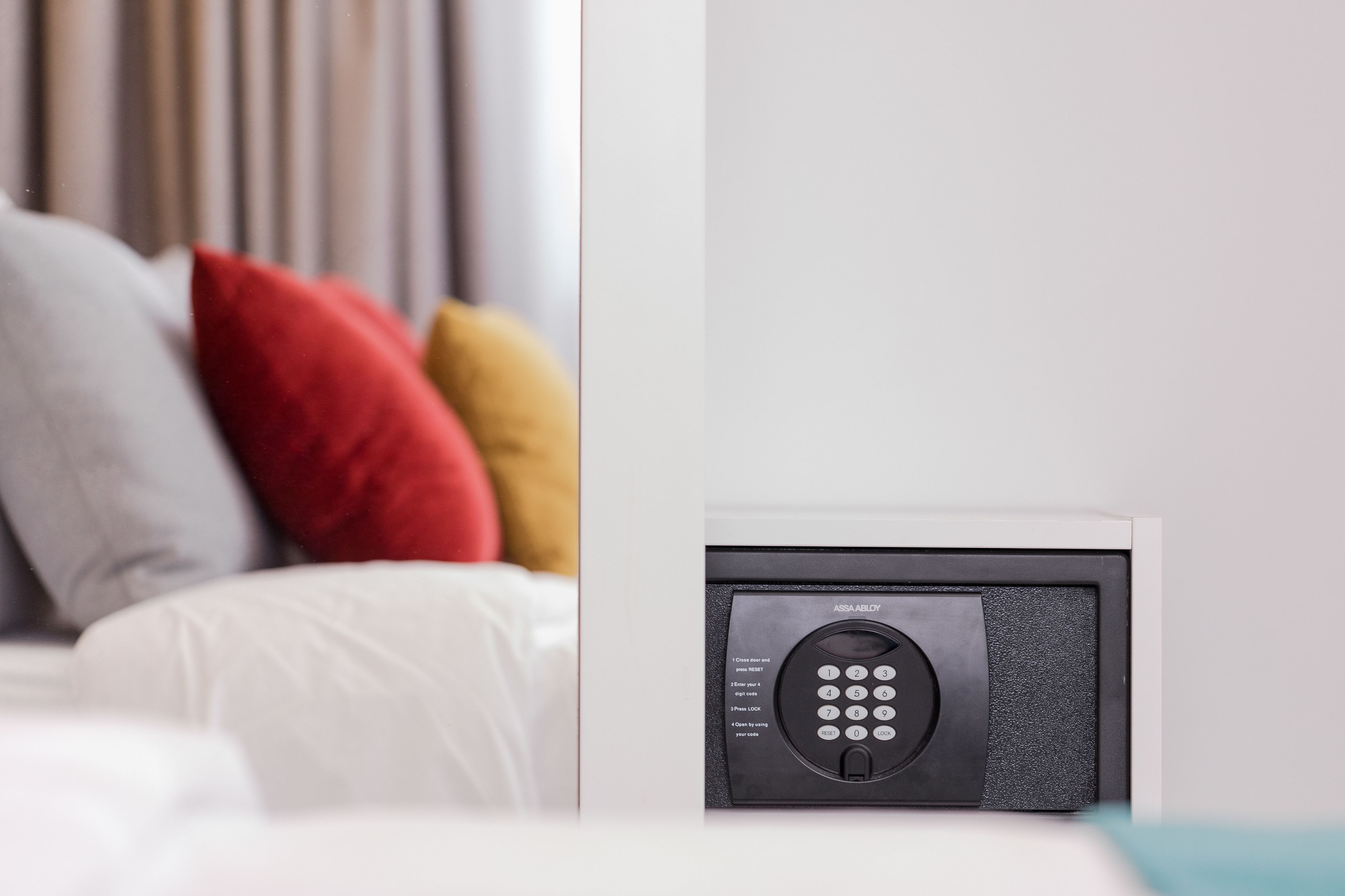 A modern, minimalist room with a bed, pillows, and a wall-mounted electronic device.