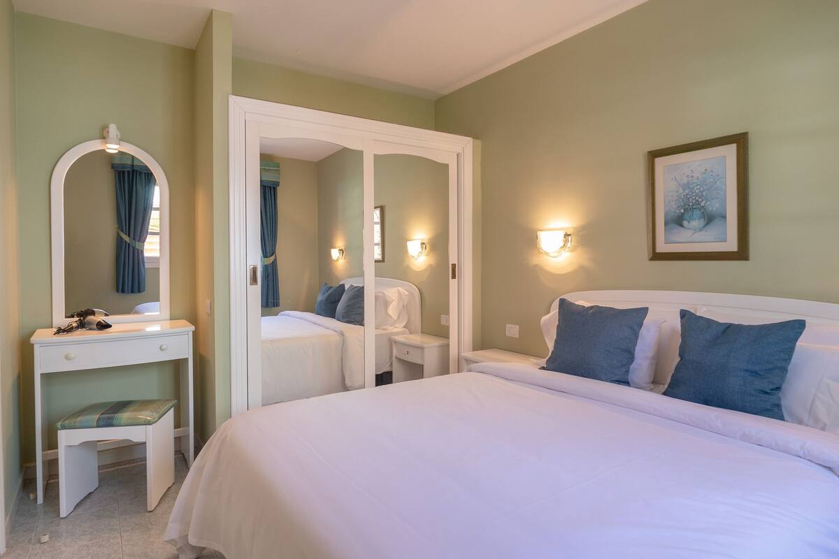 Ein Schlafzimmer mit einem Bett, einem Nachttisch, einem Spiegel und einer Wandleuchte.