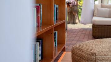 A wooden bookshelf with books, a wicker ottoman, and a view of a garden with a tree and flowers.