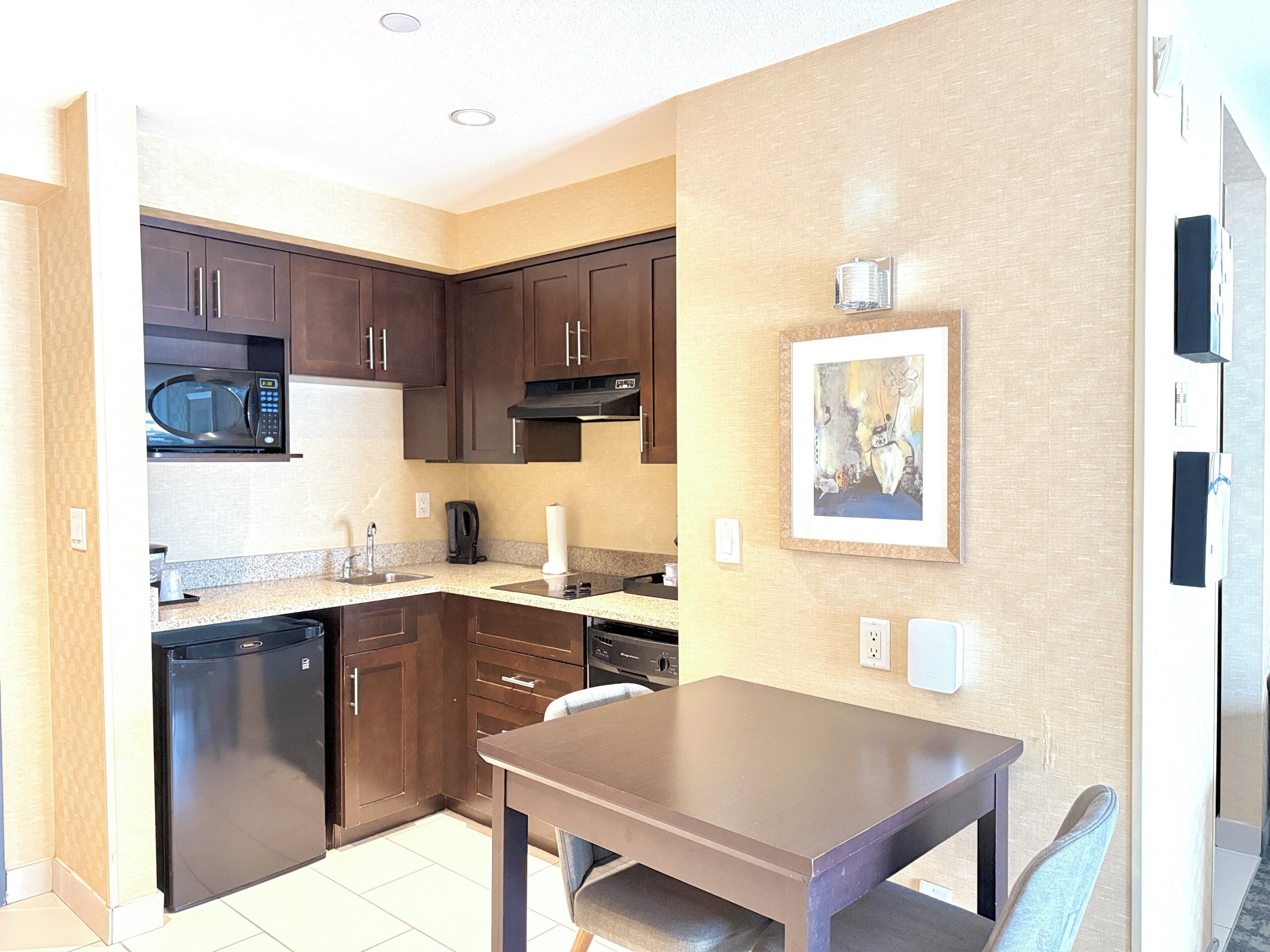A compact kitchen with dark wooden cabinets, a microwave, a stove, and a dining table with a chair.