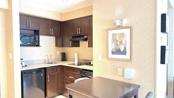 A compact kitchen with dark wooden cabinets, a microwave, a stove, and a dining table with a chair.