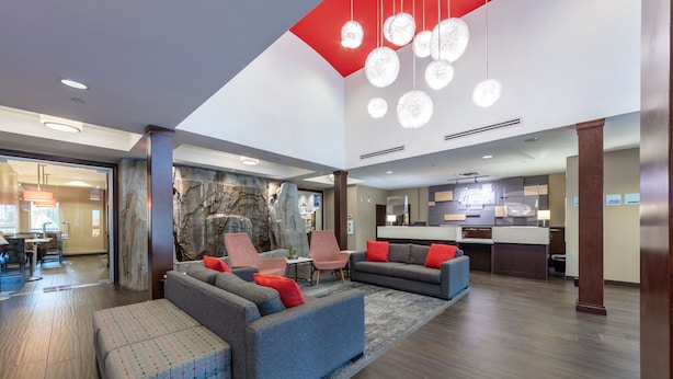 A spacious lobby with a modern design, featuring a seating area with sofas and chairs, a stone accent wall, and a kitchen area in the background. - Holiday Inn Express Hotel & Suites Riverport Richmond by IHG (Richmond)