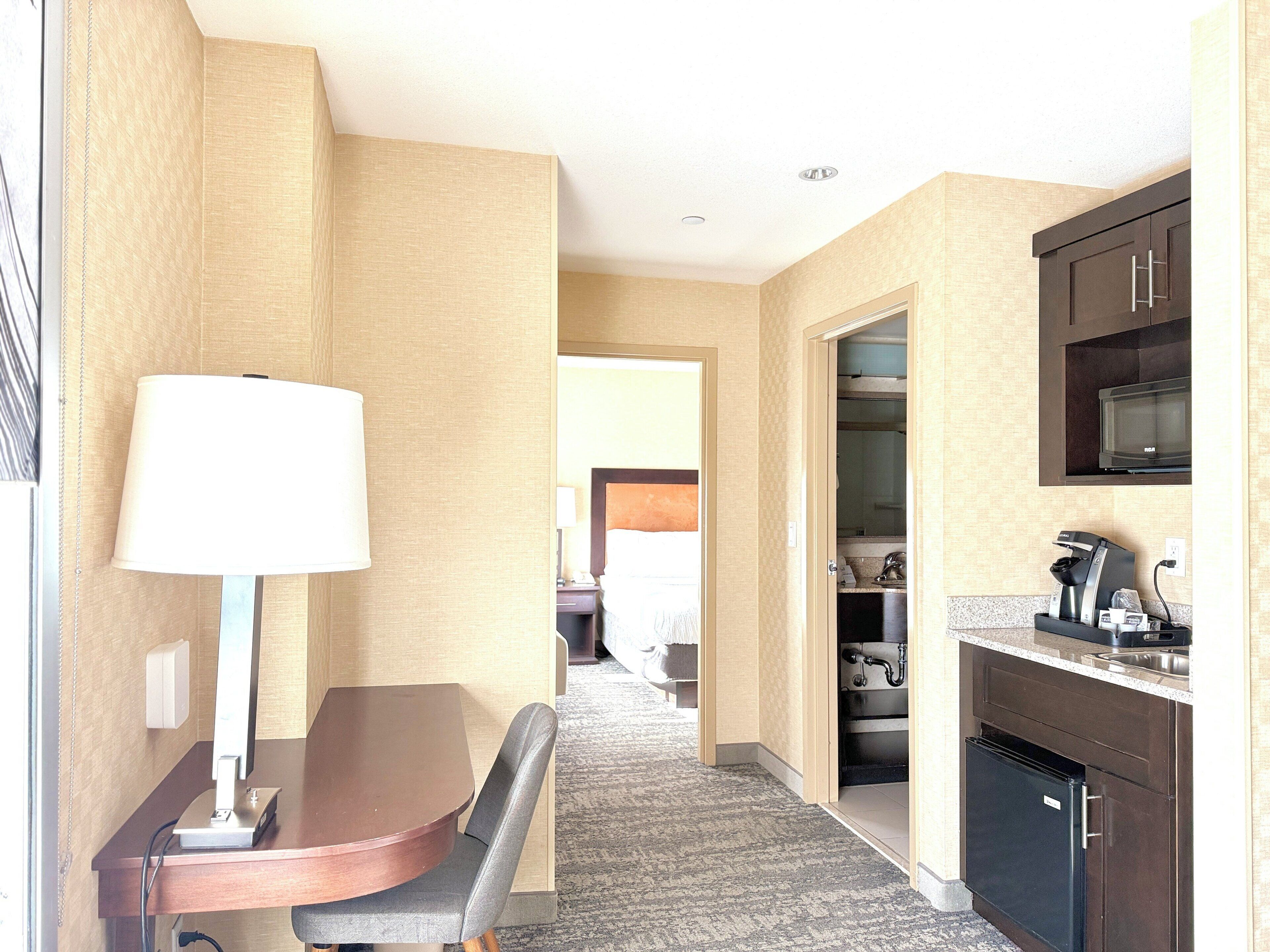 A hotel room with a dining table, a lamp, a microwave, and a coffee machine.