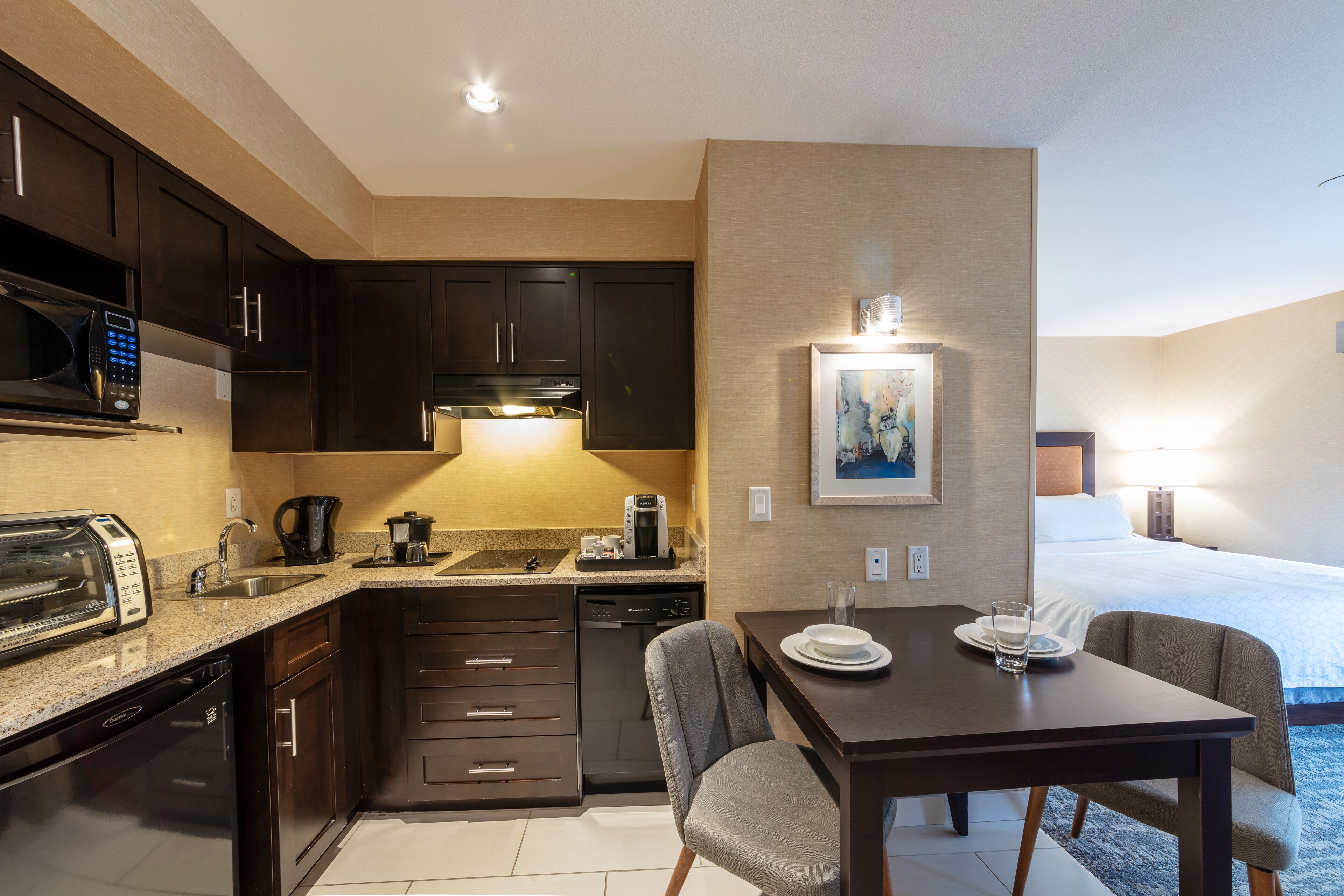 A compact hotel room with a kitchenette, a dining area, and a bed.