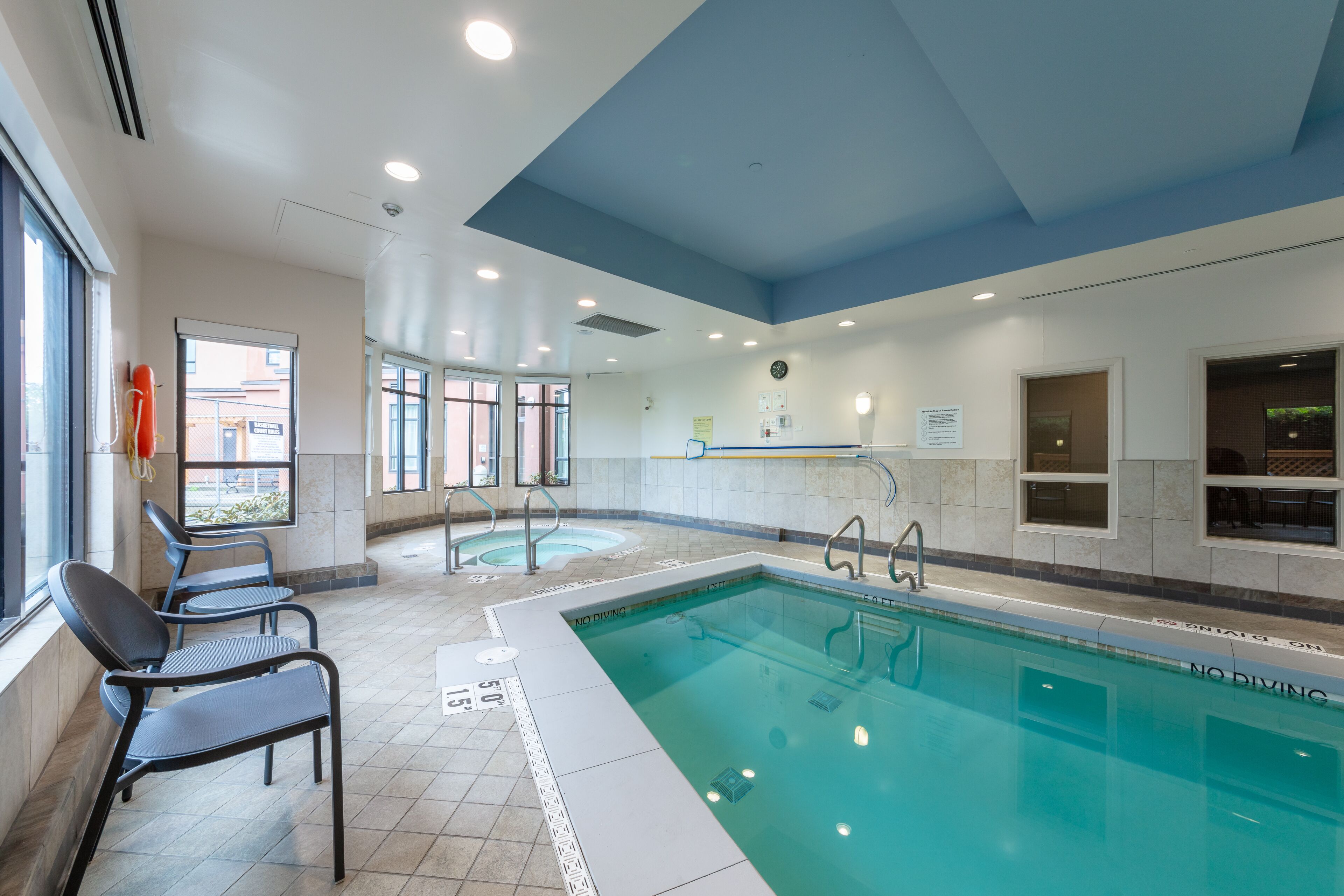 Une piscine avec un panneau indiquant qu’il est interdit de plonger, une horloge au mur et une fenêtre donnant sur l’extérieur.