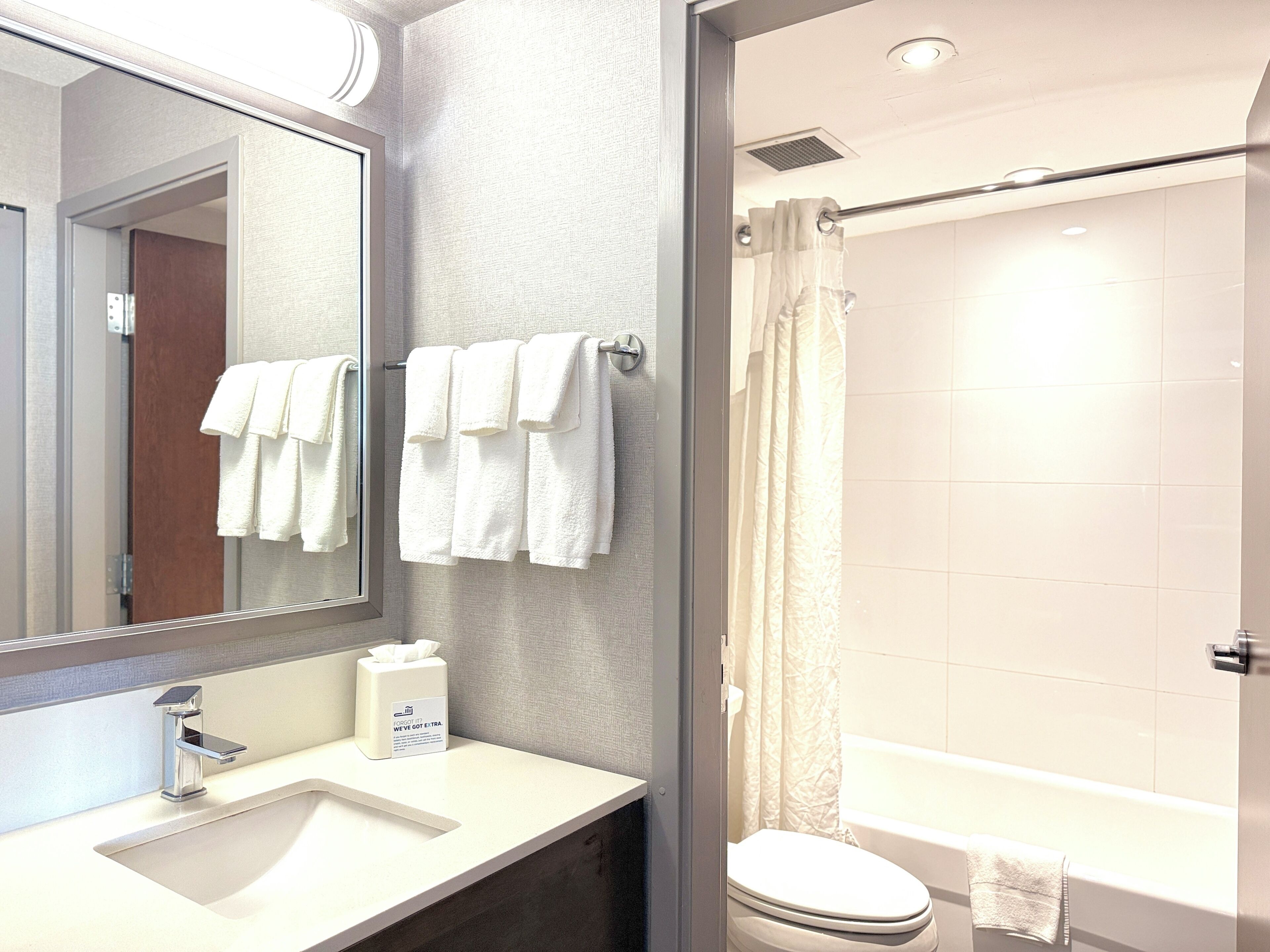 Une salle de bain équipée d’un lavabo, d’un miroir, d’un porte-serviettes, de toilettes et d’un rideau de douche.