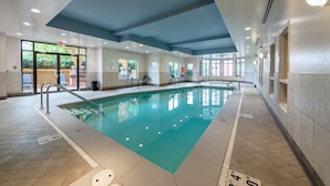 Une grande piscine intérieure à l’eau d’un bleu limpide, entourée de murs recouverts de carreaux et dotée d’un plafond avec des luminaires encastrés.