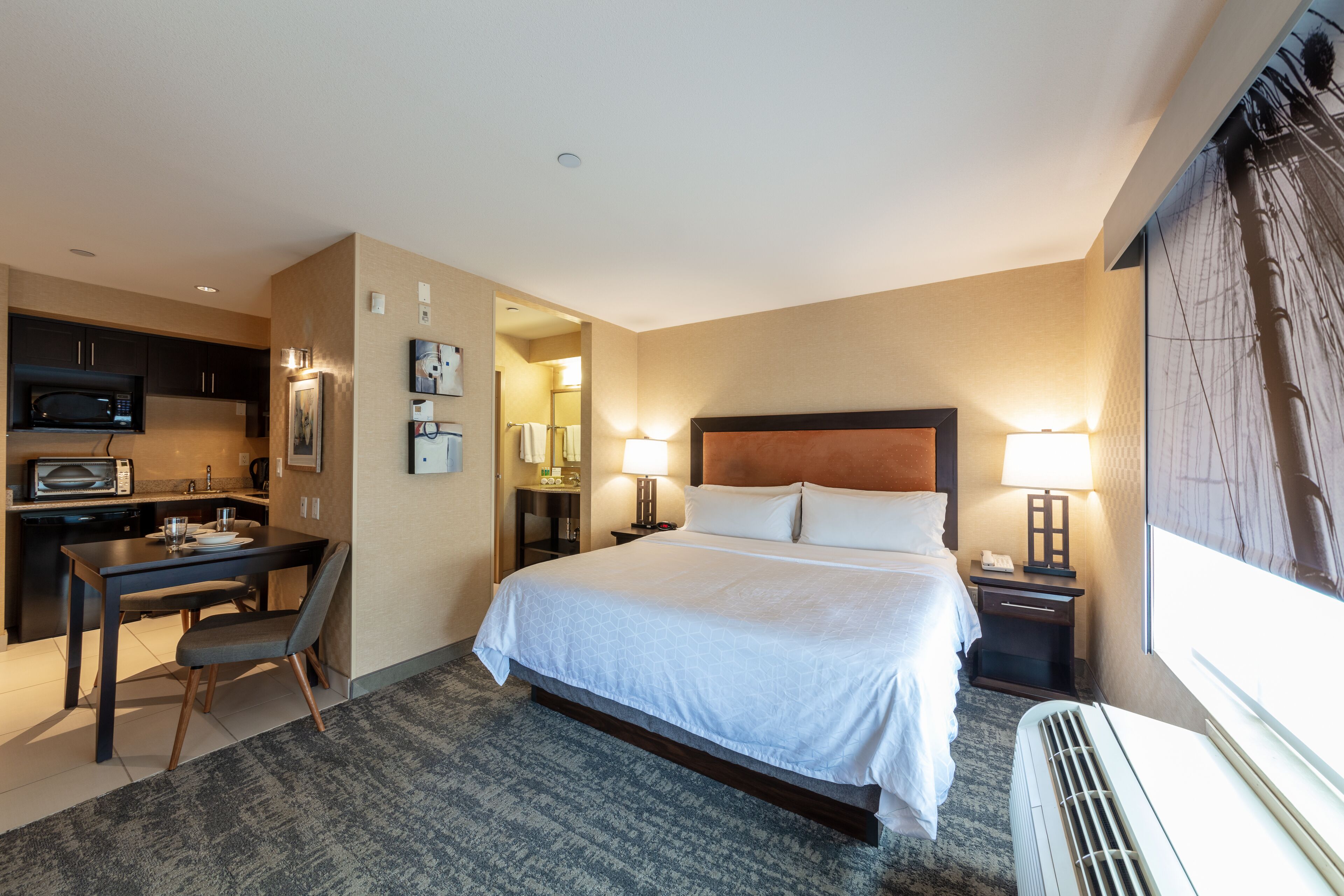A hotel room with a bed, desk, and kitchenette.