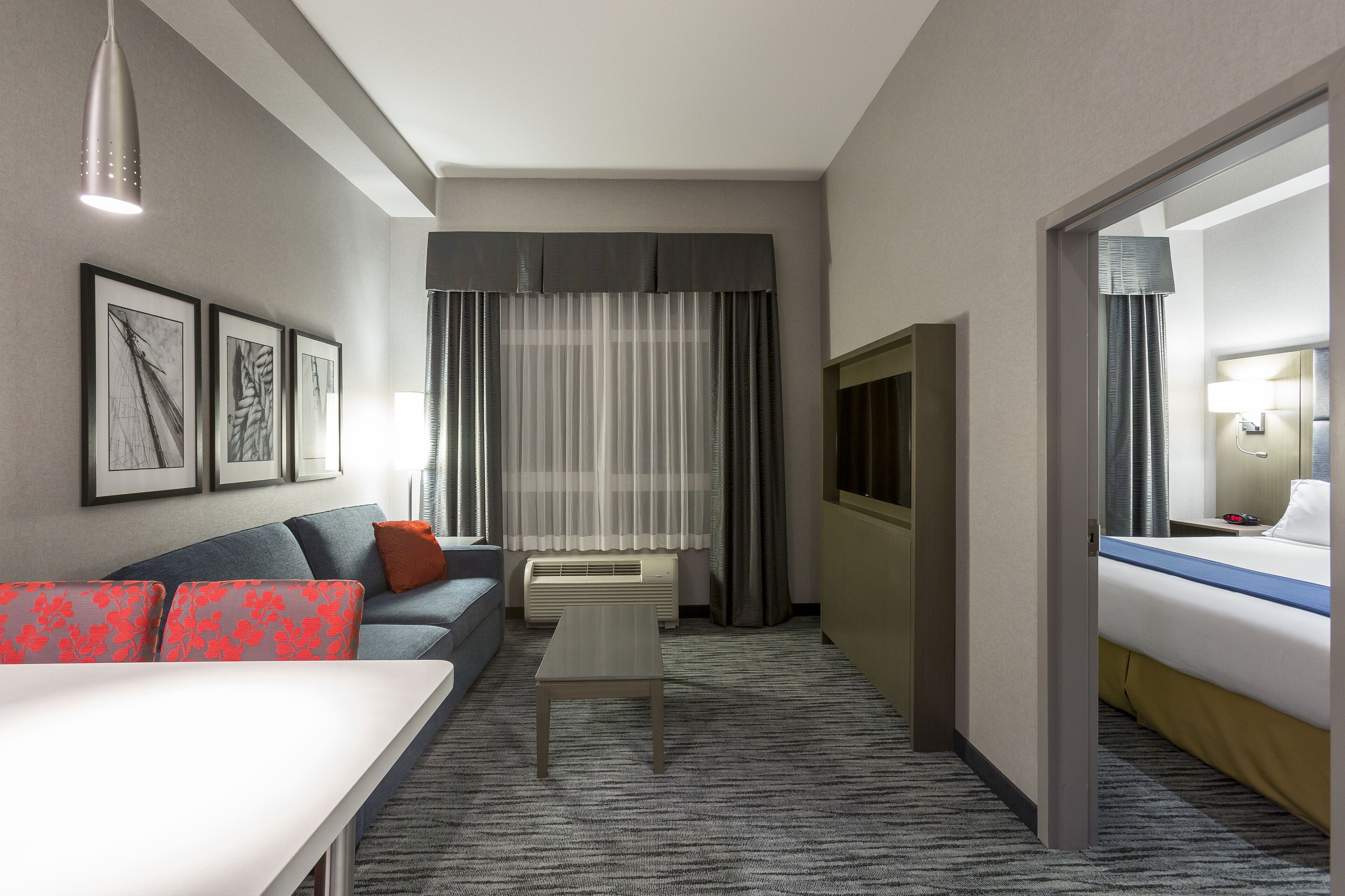 A hotel room with a sofa, a small table, a bed, a TV, and a window with curtains.